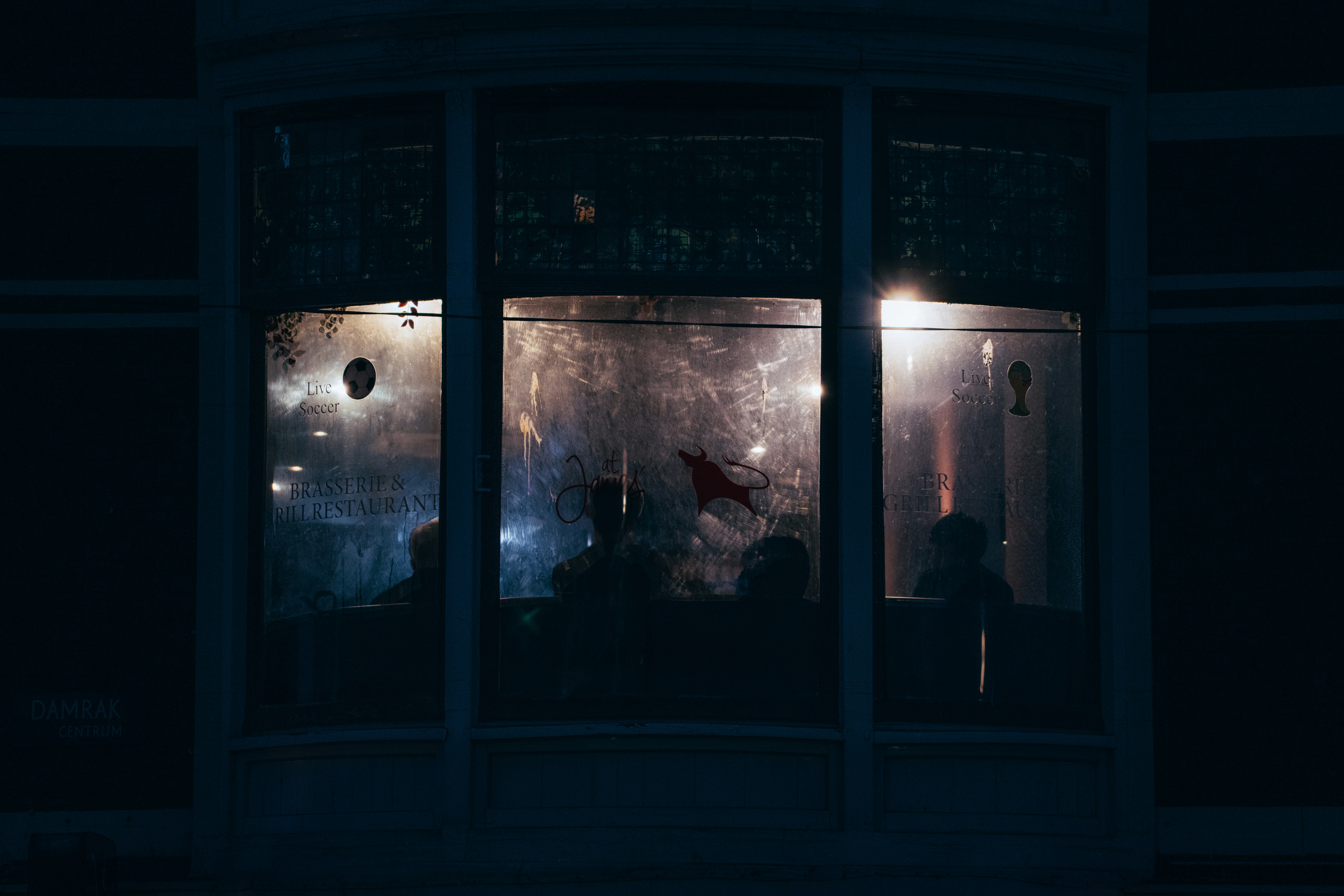 Silhouetted figures seen through a dimly lit window at night.