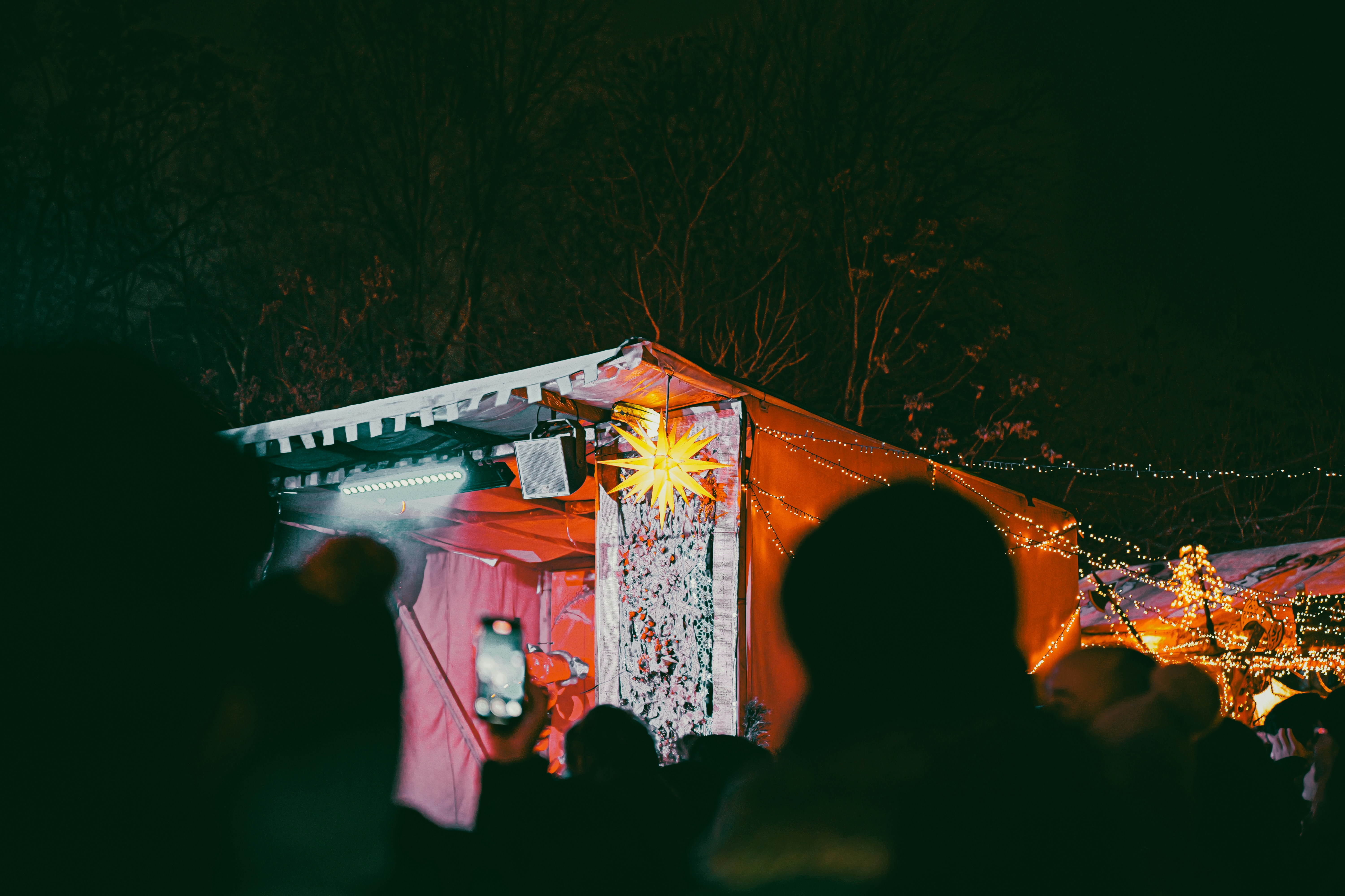 People gathered around a brightly lit stall at night. - people-gathered-around-a-brightly-lit-stall-at-night-3yfLocFym-k
