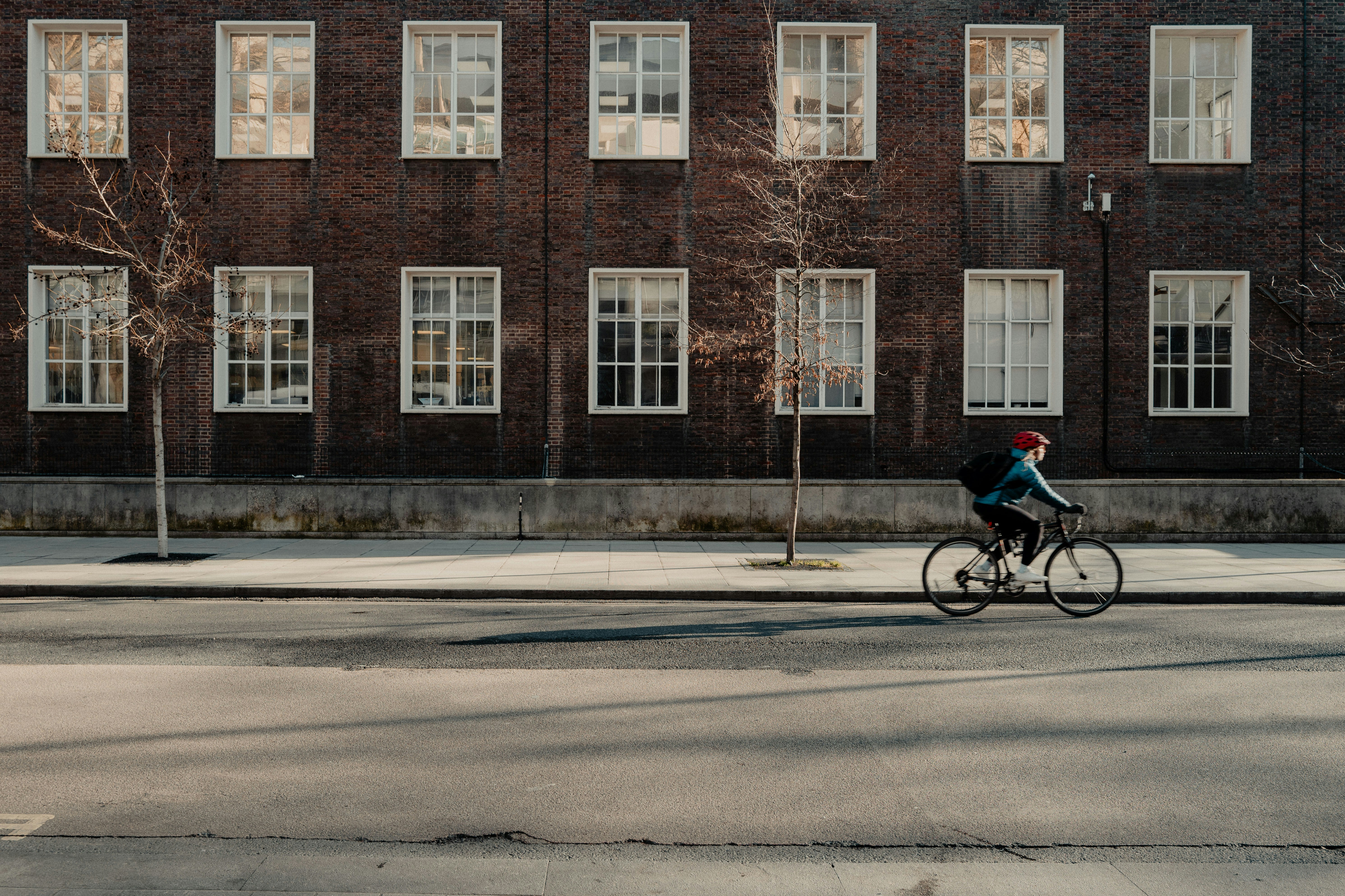 Person cycling past a brick building with many windows.