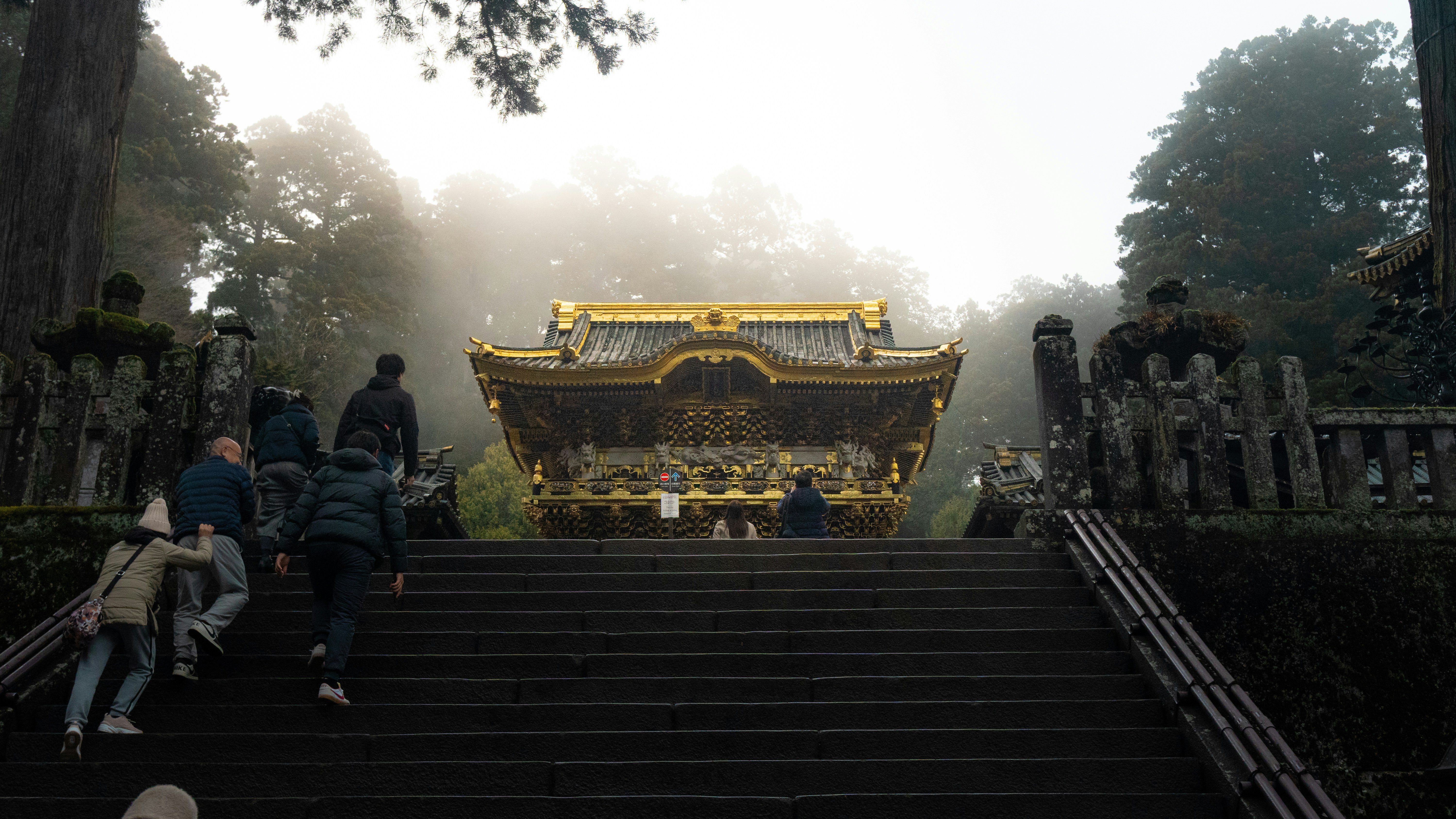 People ascend stairs to a golden japanese shrine.