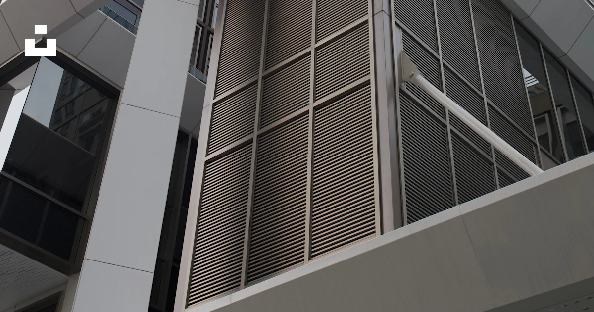A modern building with glass windows and metal louvers under a bright ...