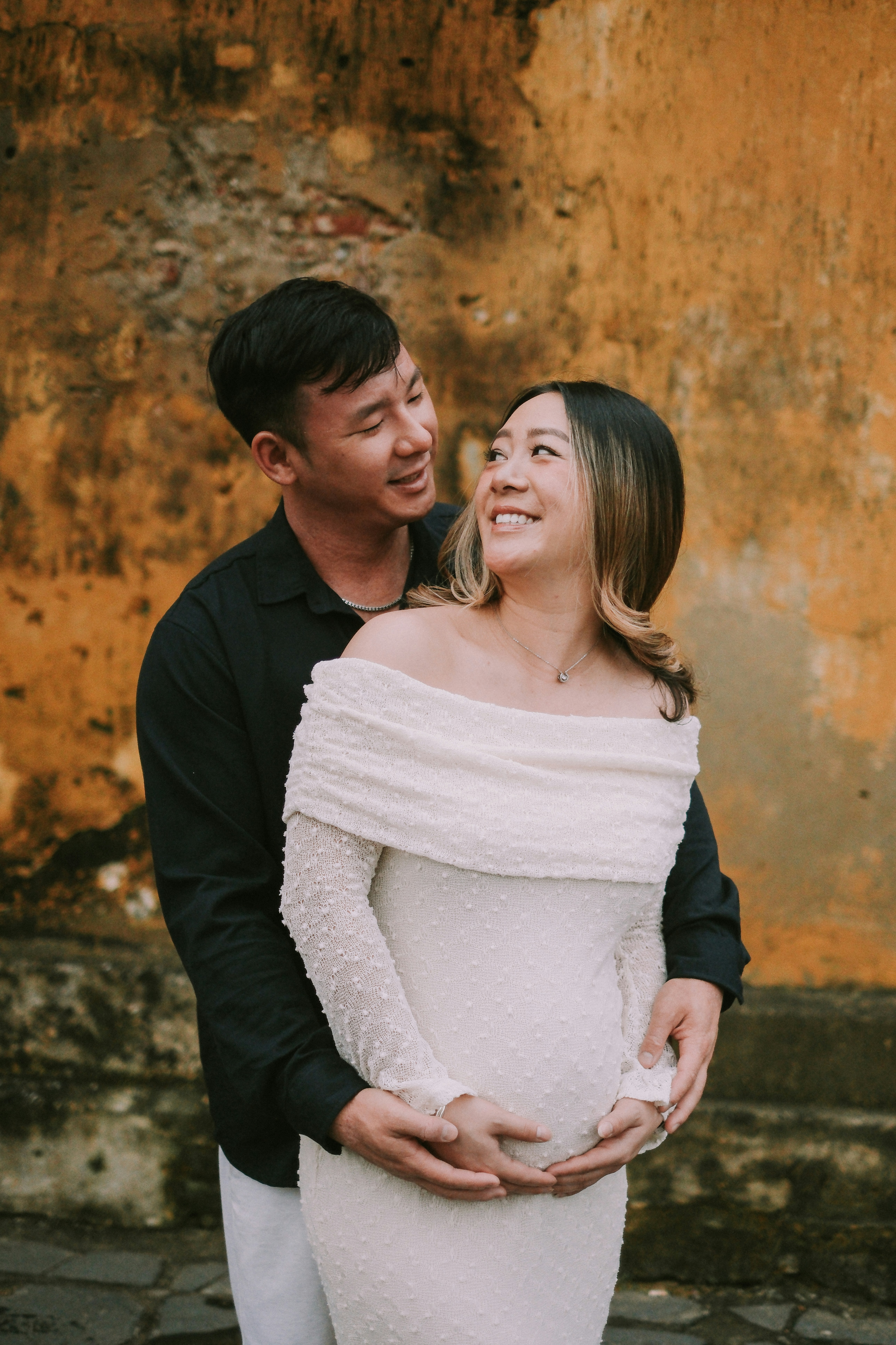 Couple embracing in front of a textured wall.