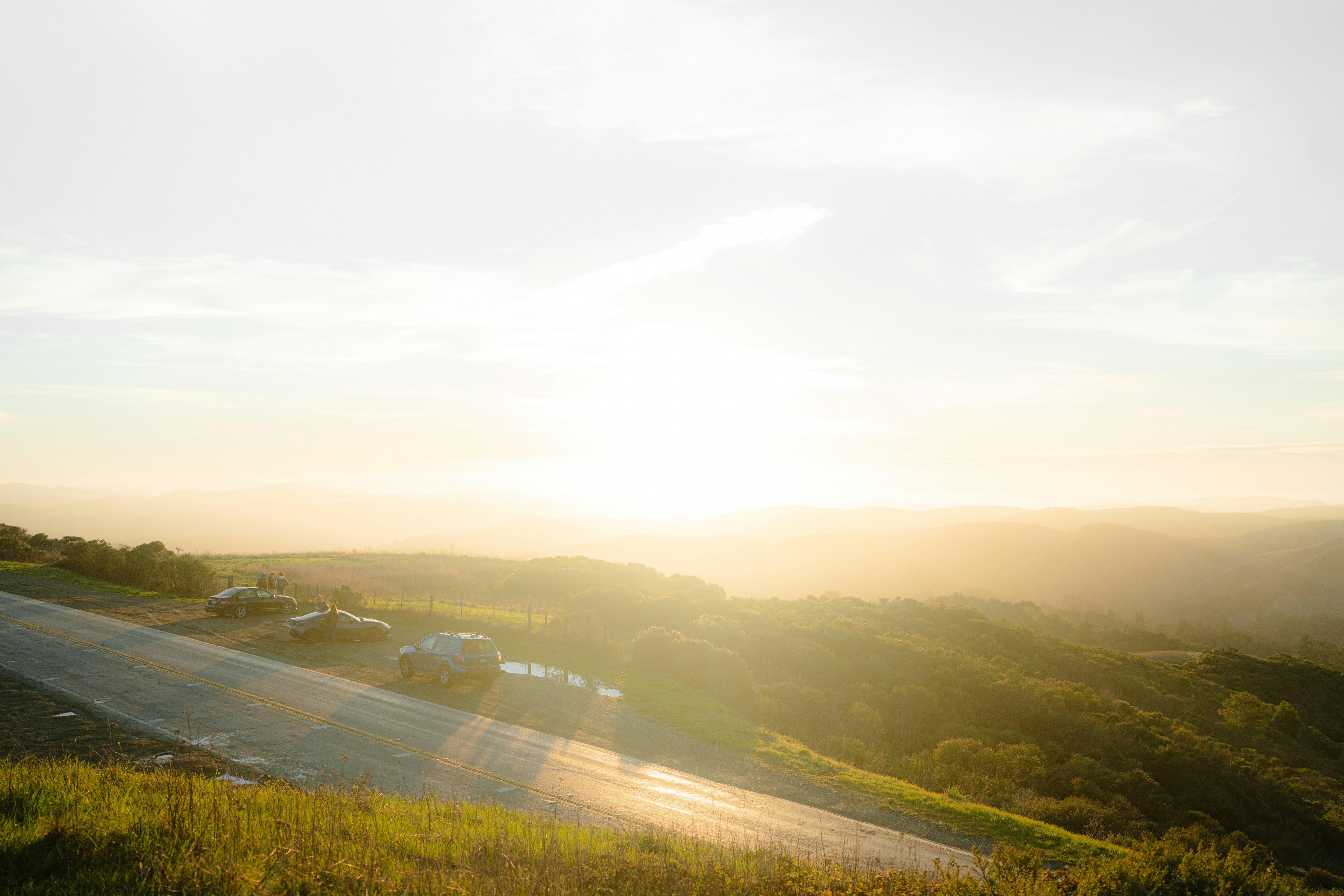 Cars on a road with a sunset over hills