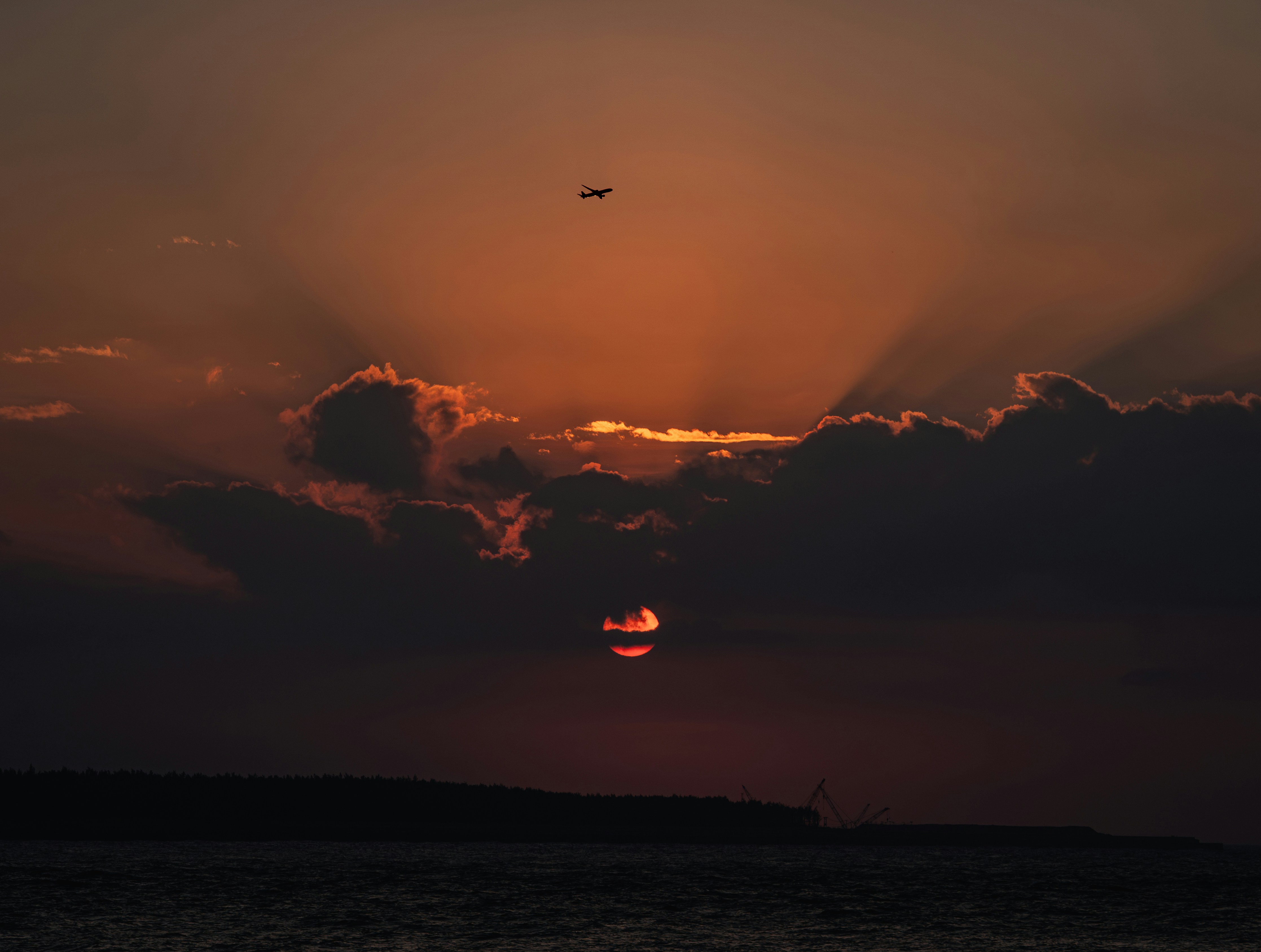 Airplane flying during a dramatic sunset over water.