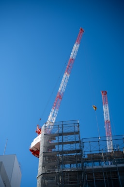 Two construction cranes against a clear blue sky.