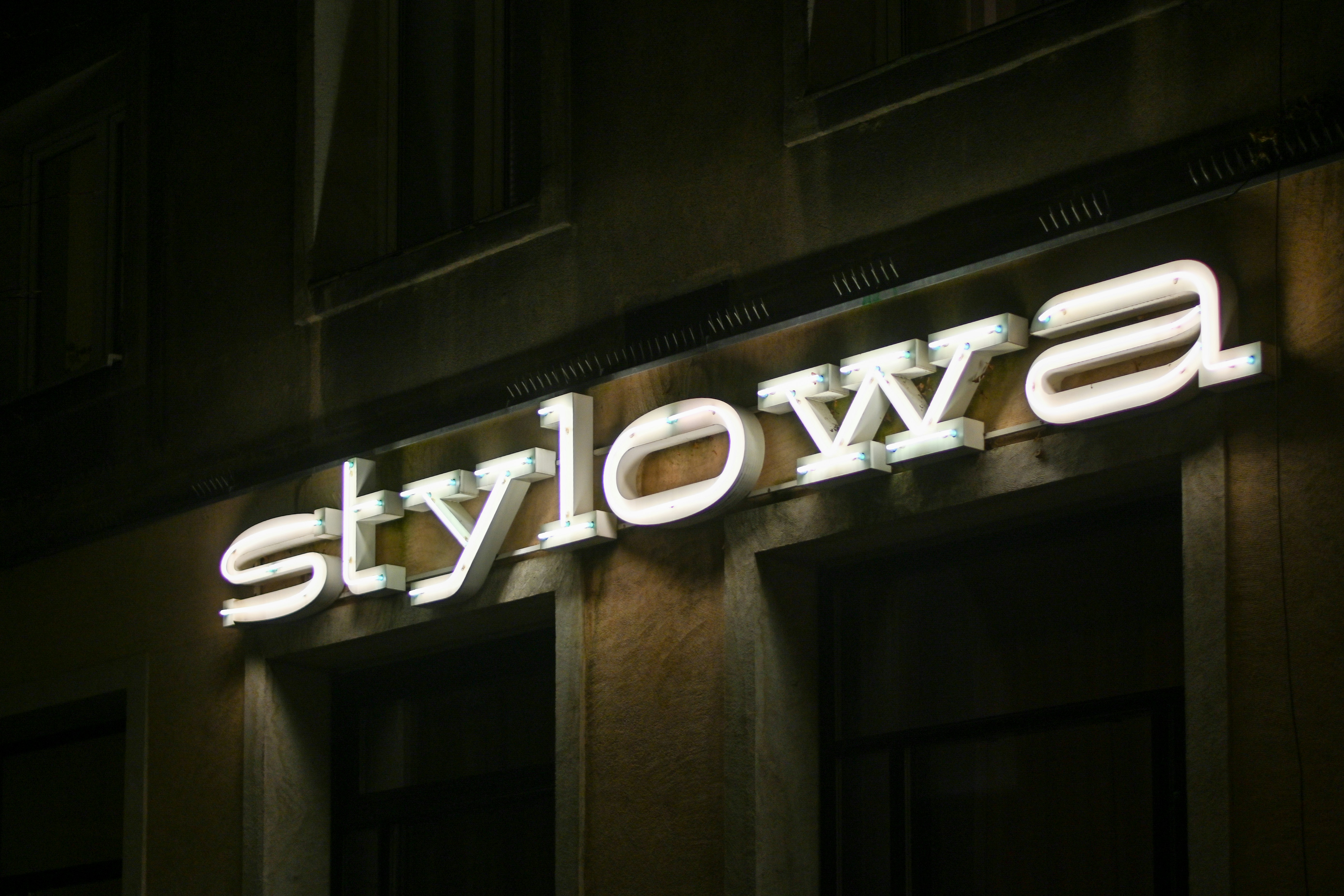 Lit sign spelling 'stylowa' on building at night