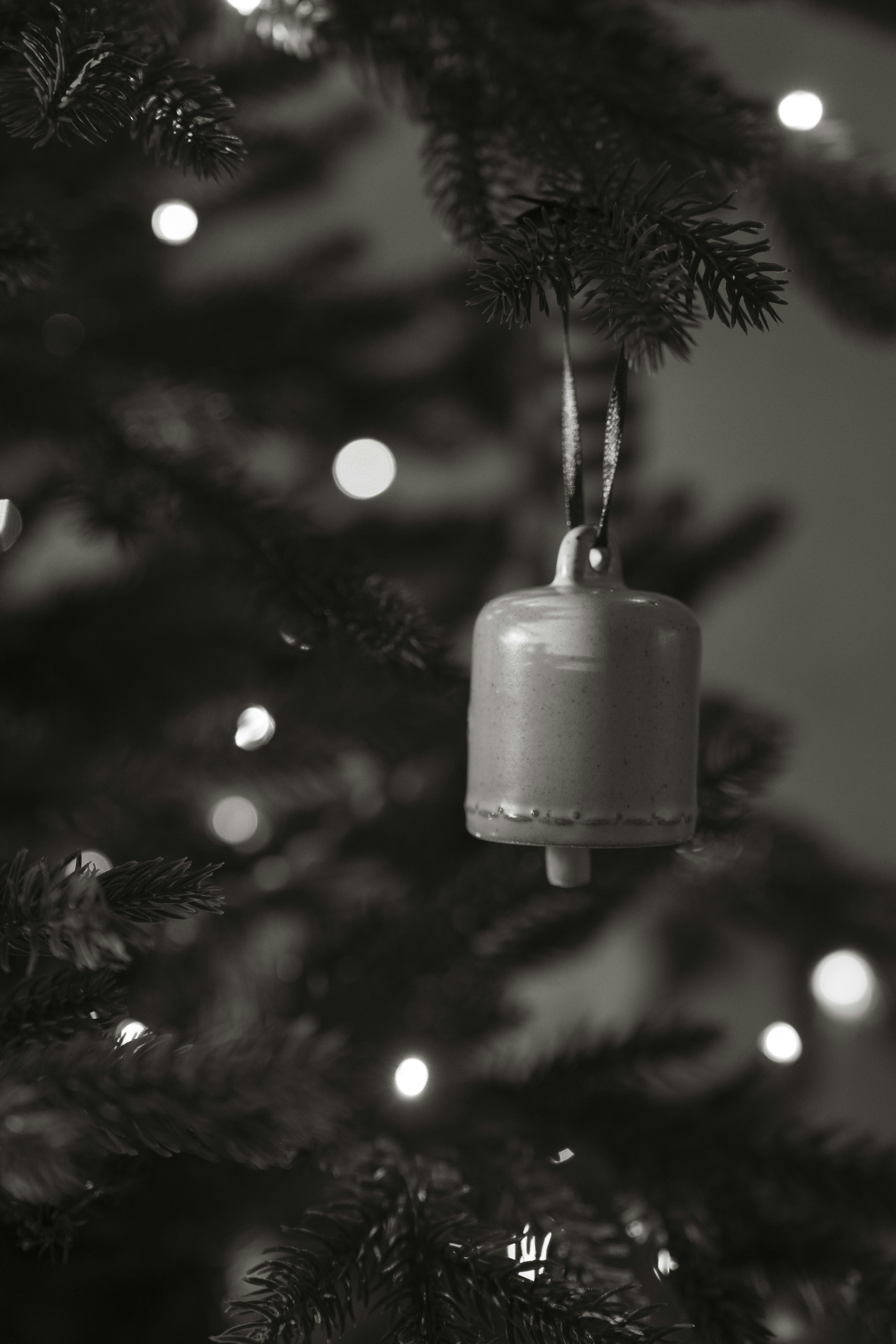 A single bell ornament hangs on a christmas tree.