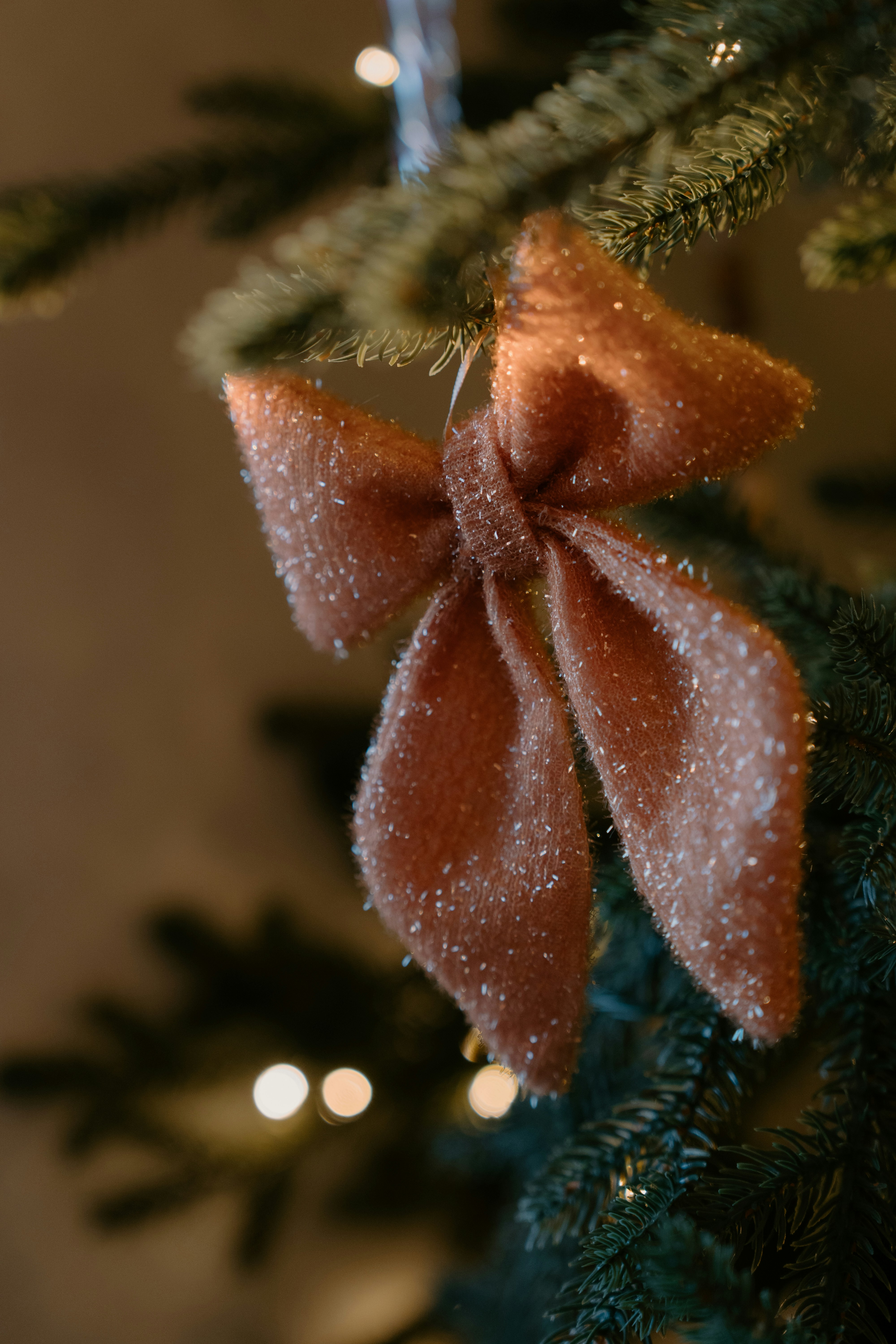 A sparkly rose gold bow ornament on a christmas tree.