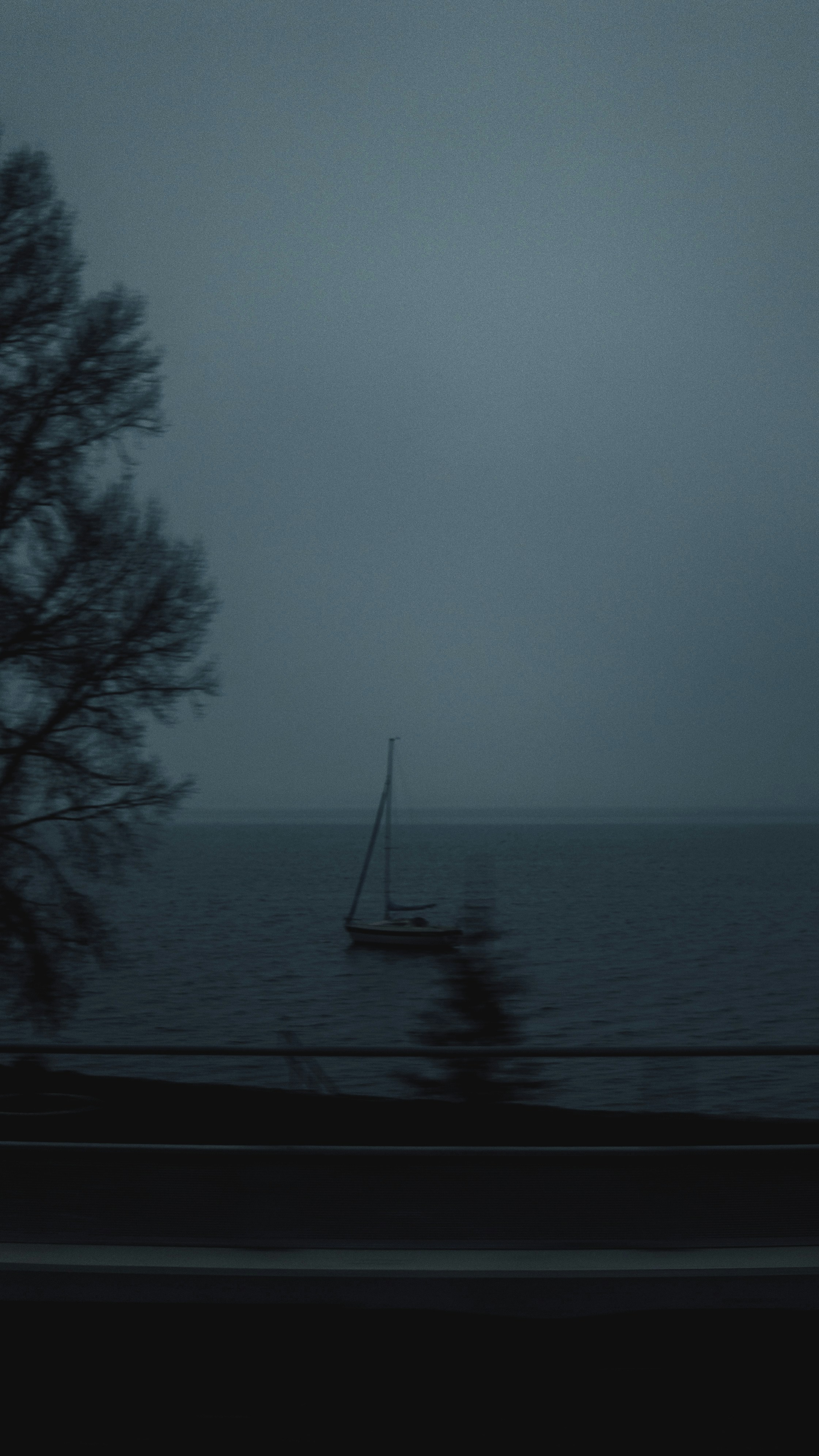 A lone sailboat on a dark, foggy body of water.