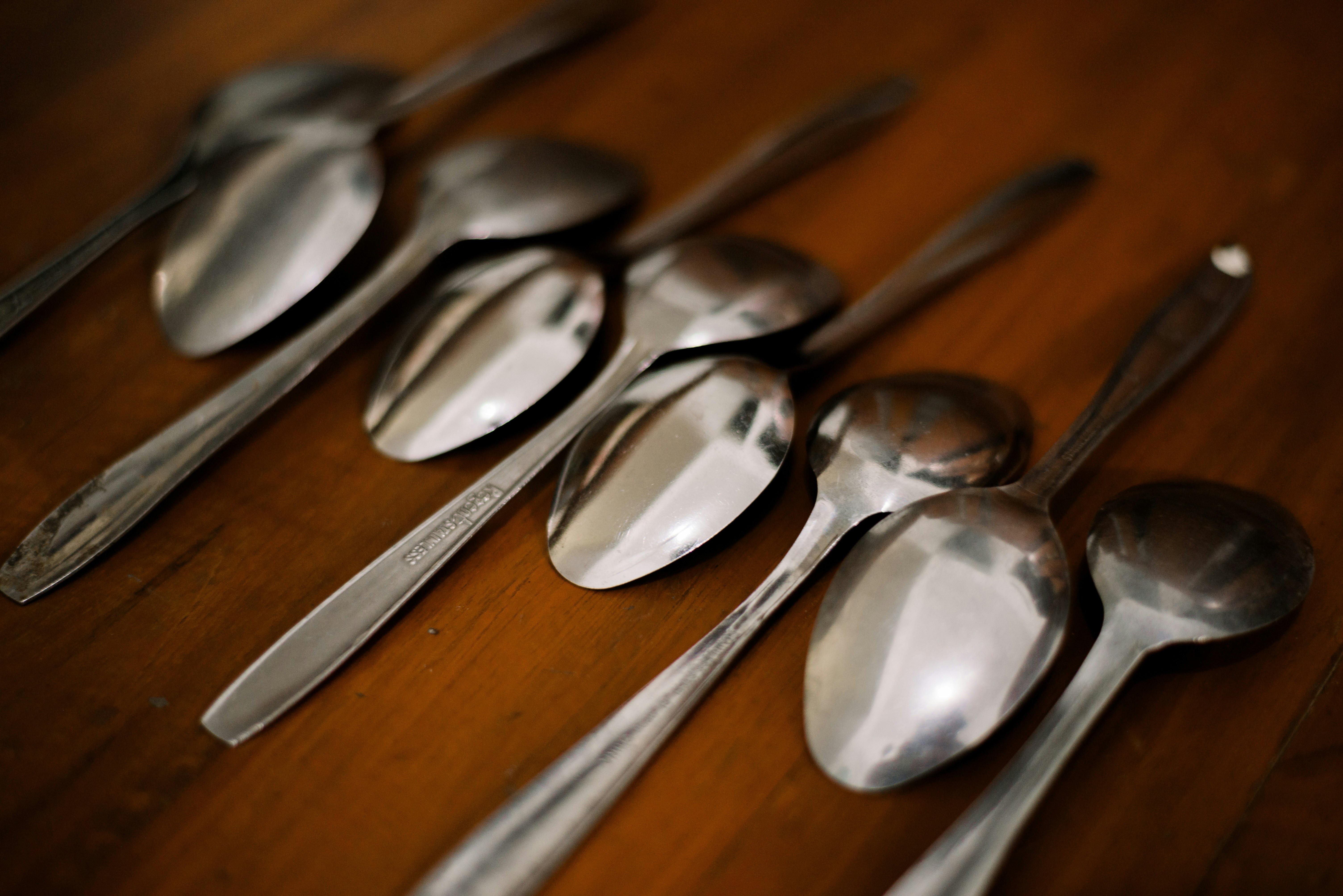 Several shiny metal spoons arranged on a wooden surface
