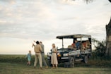 People gathered around a safari vehicle in a grassy field.