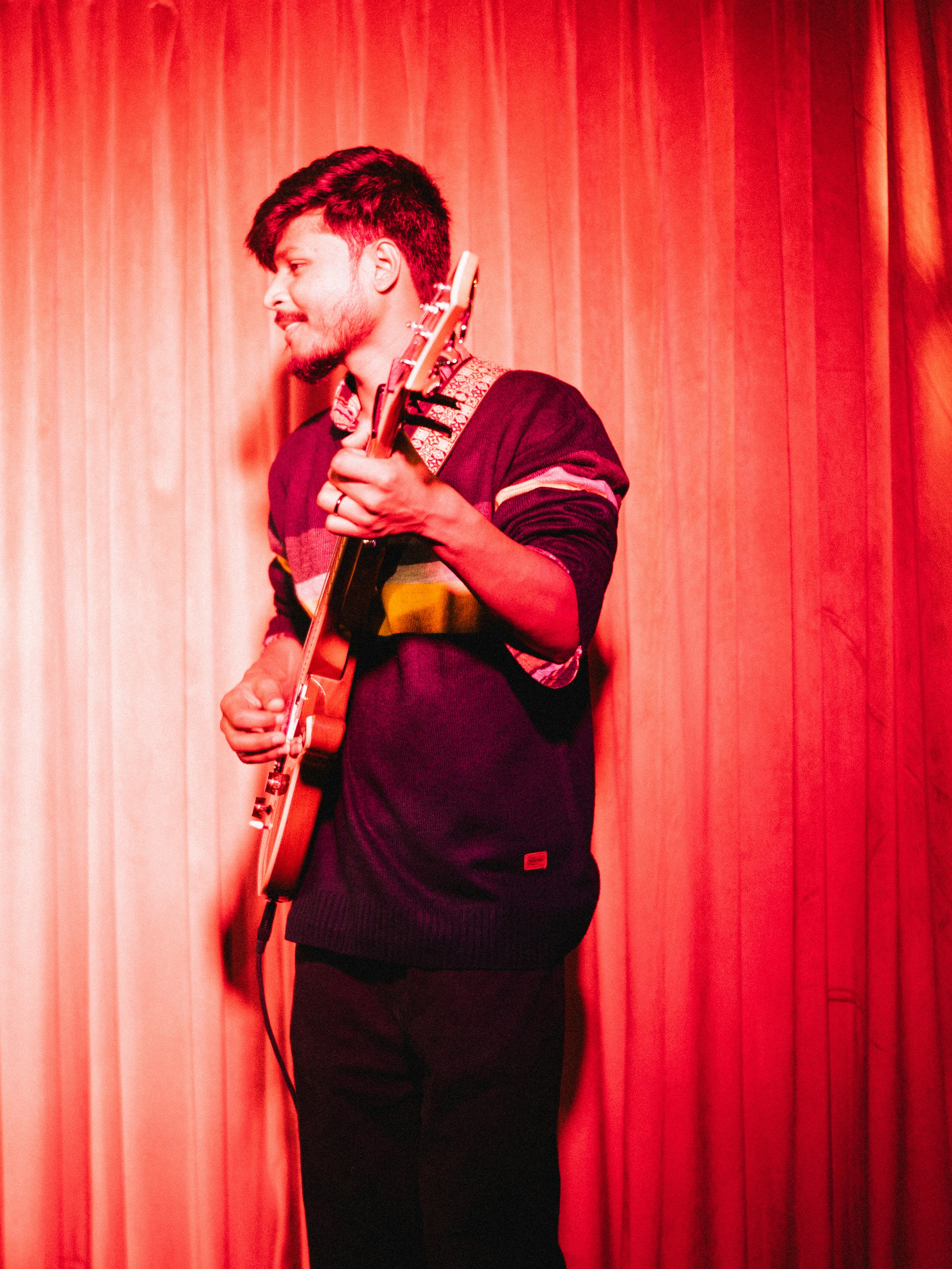 Man playing guitar on stage with red curtain background