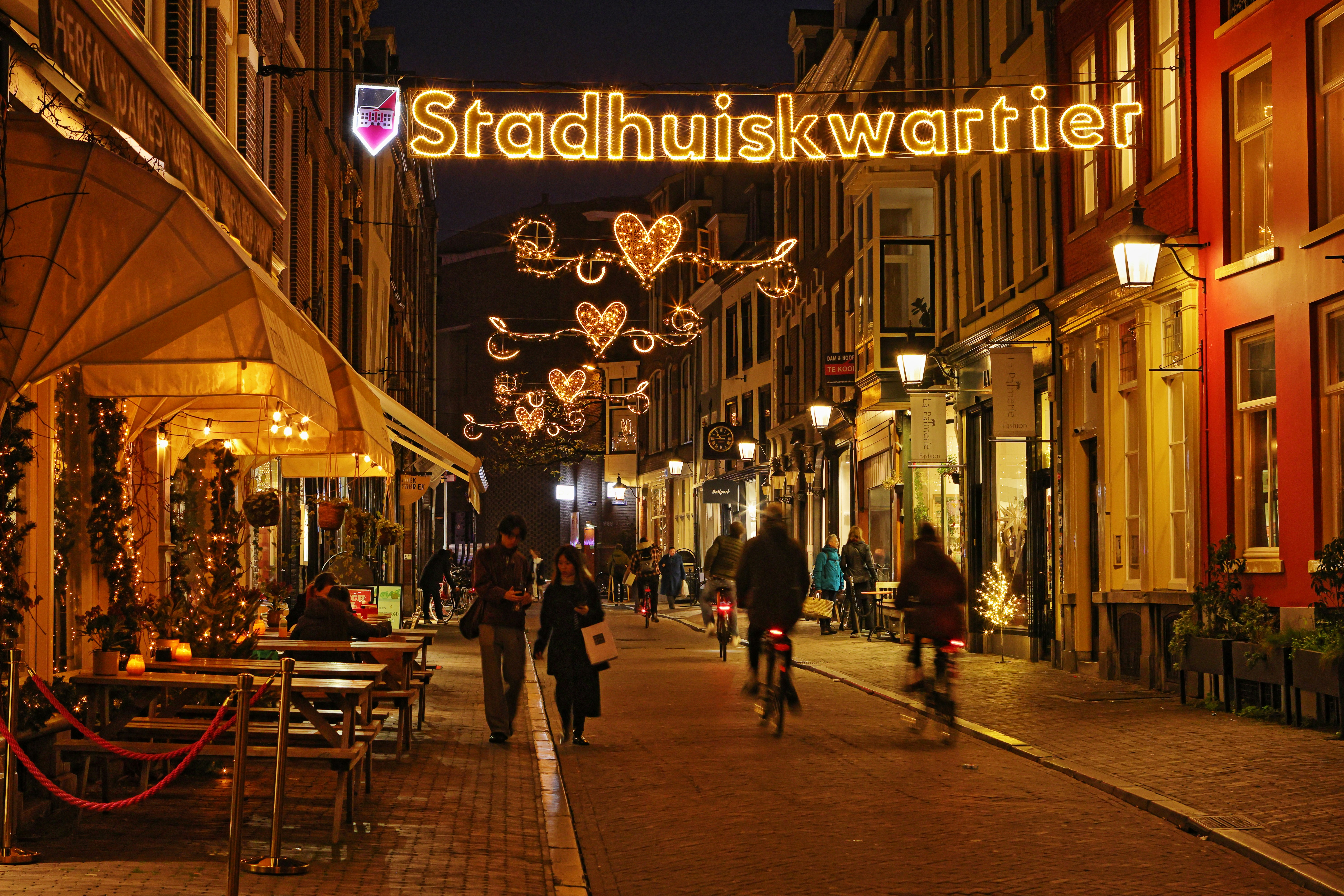Pessoas caminhando e pedalando em uma rua decorada à noite.
