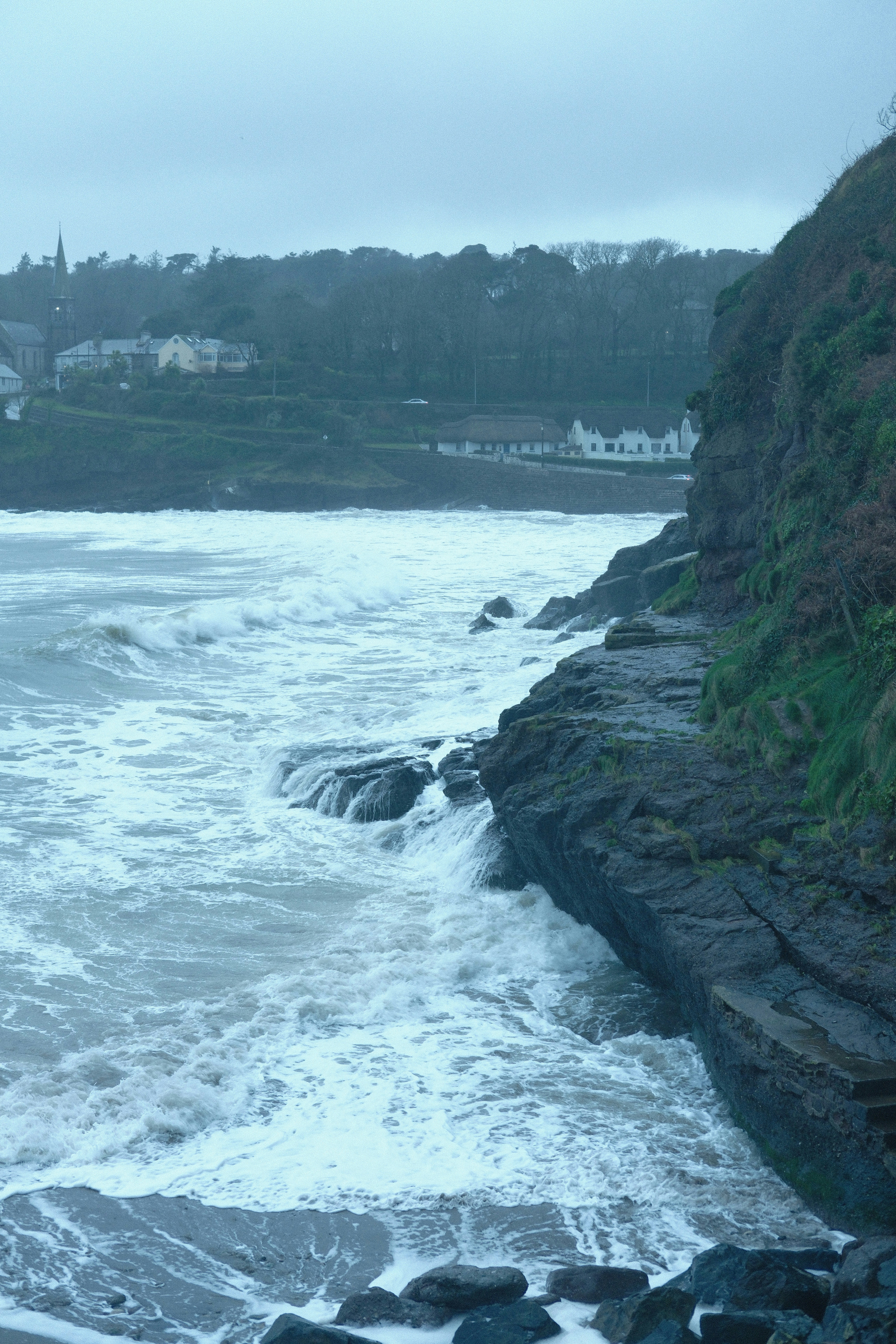 Las olas rompen contra la costa rocosa con trasfondo de pueblo costero