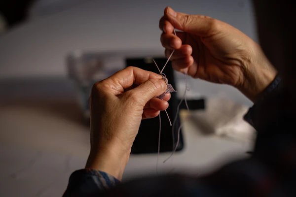 Hands threading a needle in warm light
