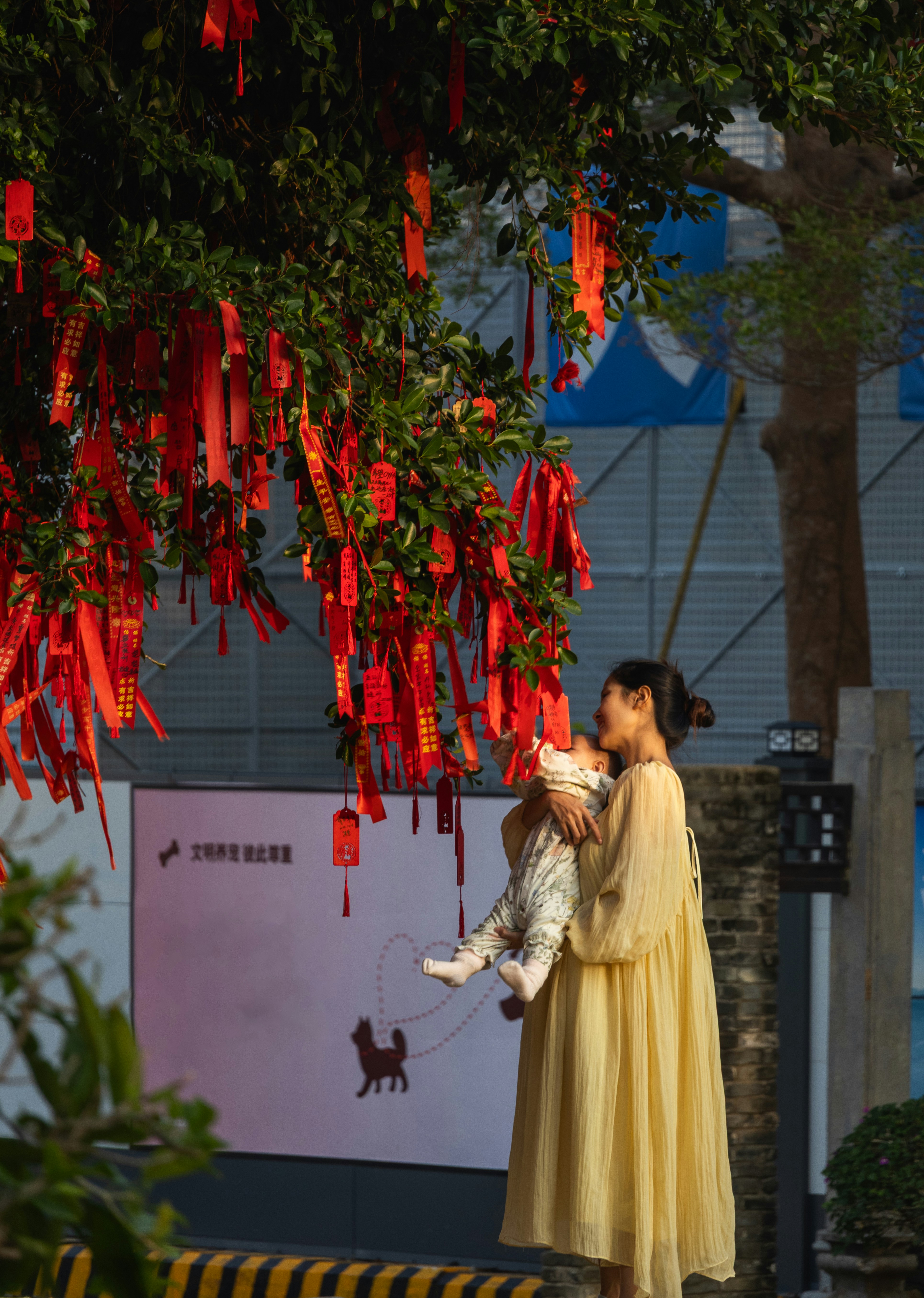Woman holding baby under tree with red ribbons