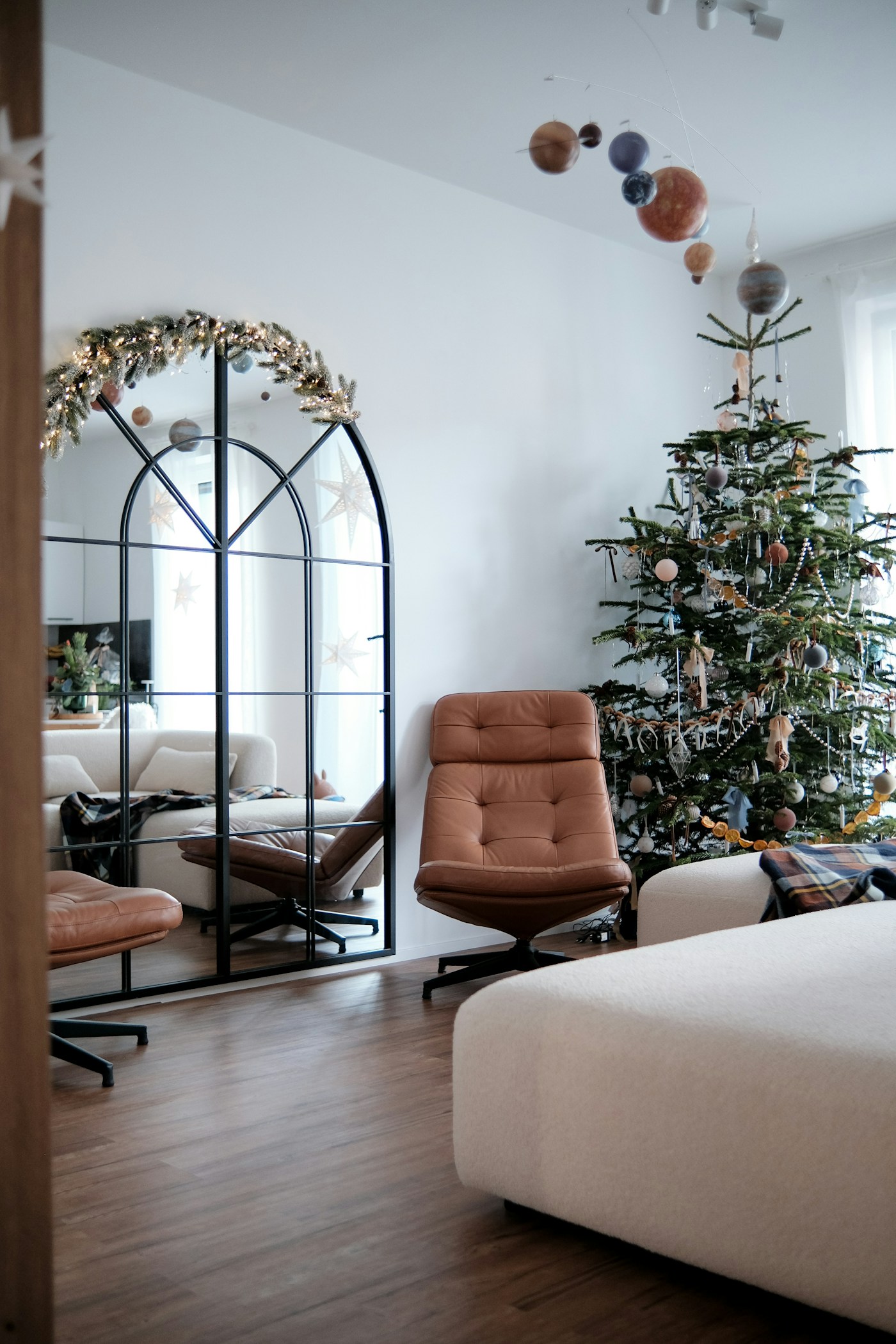 A Christmas tree beside brown leather chairs, pale upholstery and softly colored ornaments.