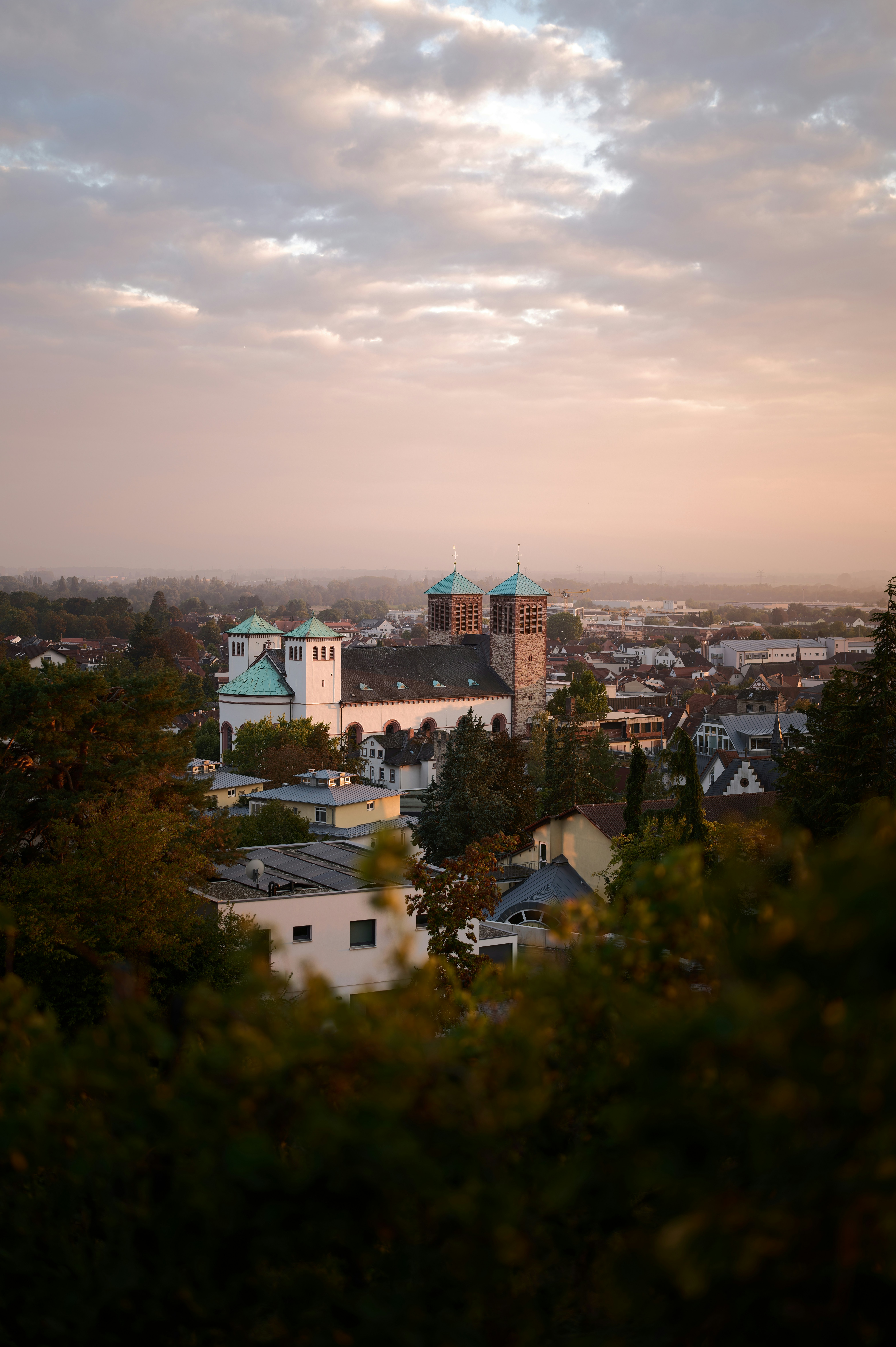 A church with green roofs overlooks a town at dusk.