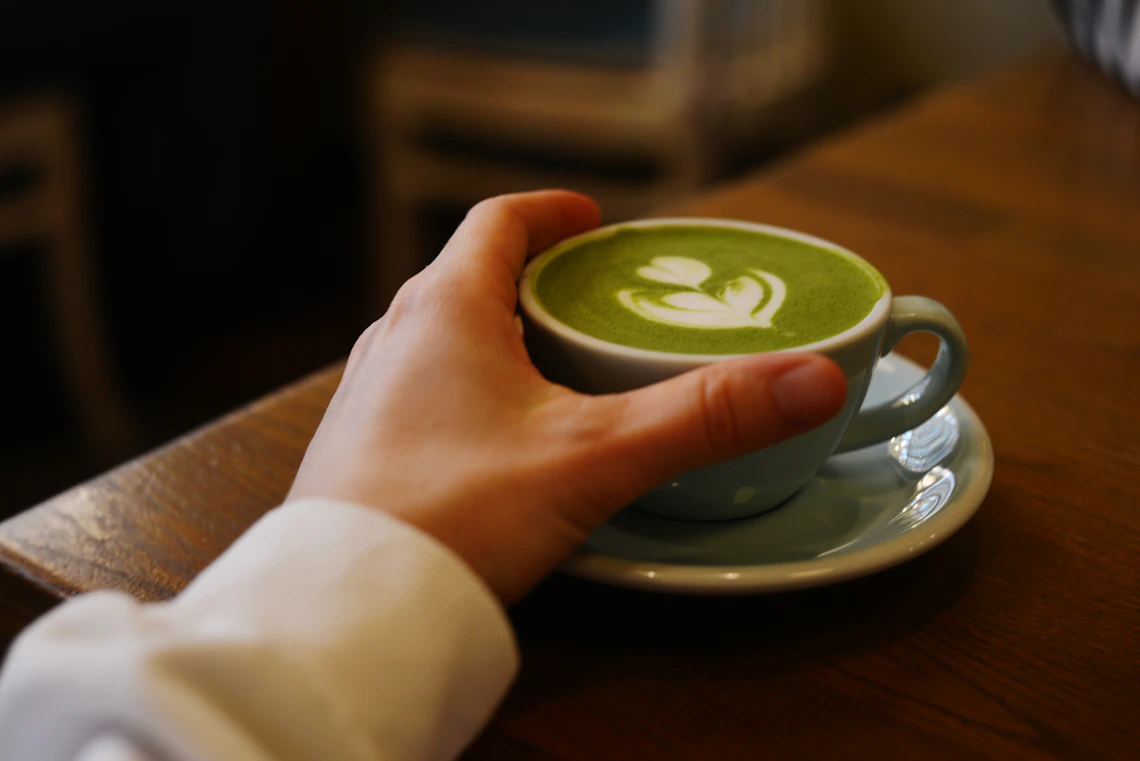 Hand holding a freshly prepared matcha latte