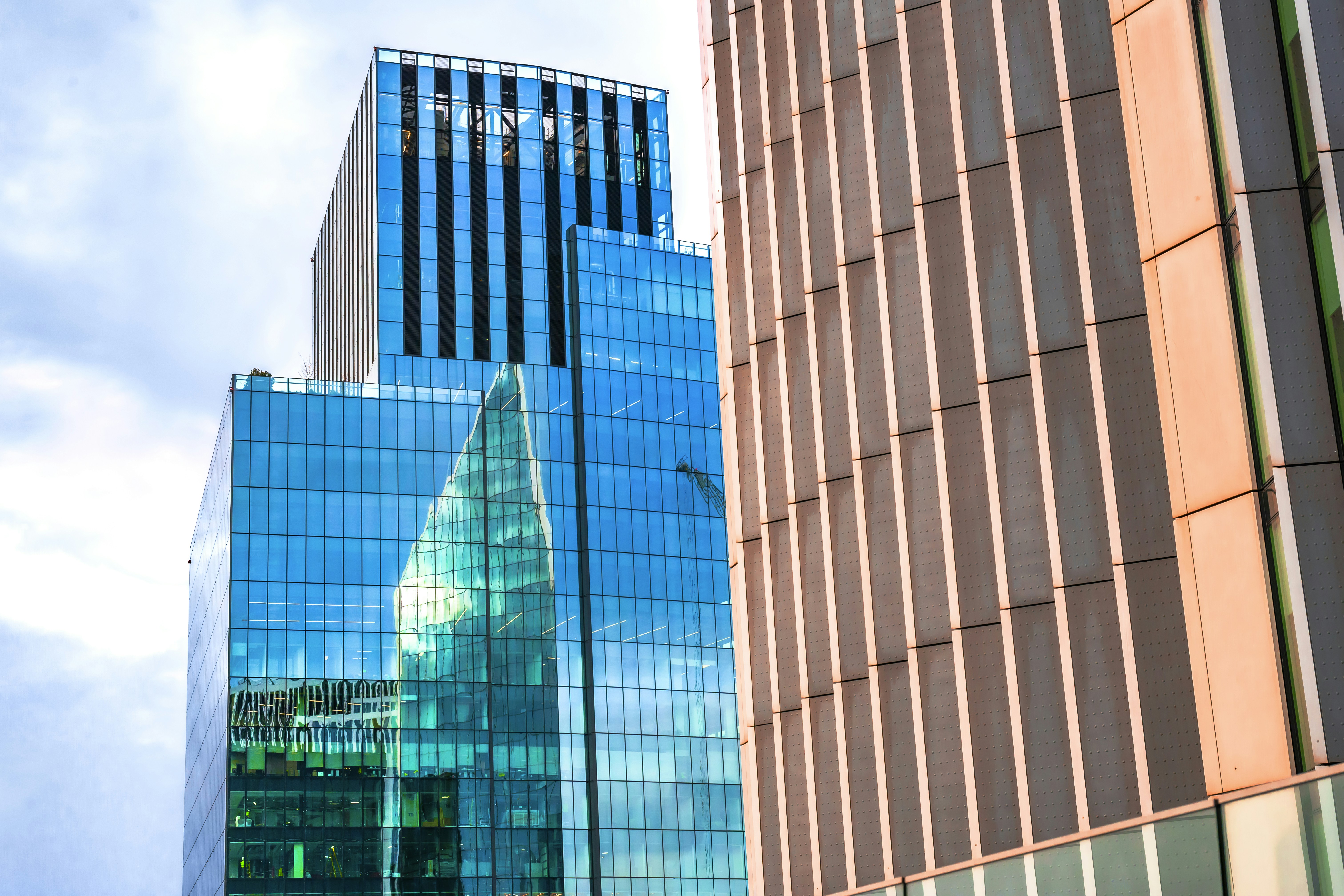 Modern glass skyscrapers reflecting the sky and clouds.