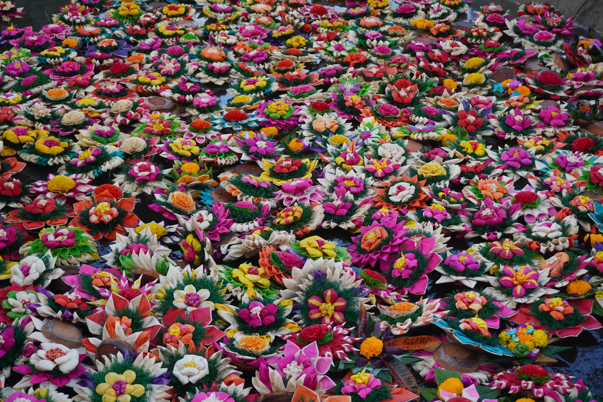 Many colorful floral arrangements floating on water.