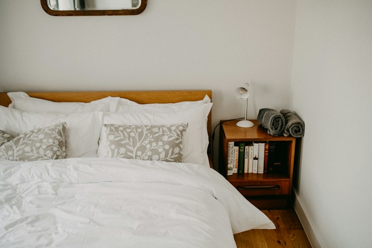 A neatly made pull-out bed with folded blankets and a reading lamp in a cozy corner