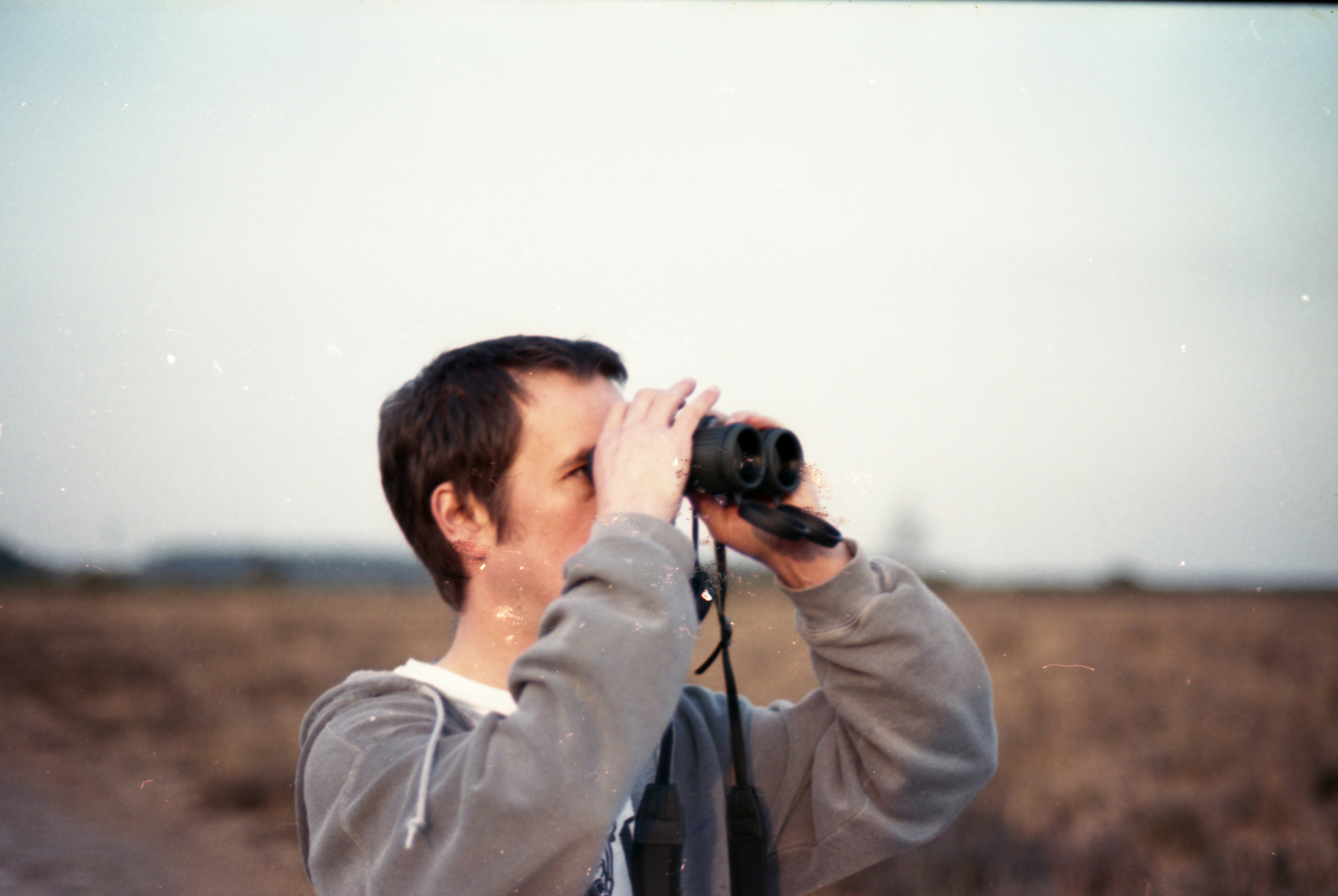 homeowner using binoculars to inspect a roof from the safety of the ground - storm damage roof inspection
