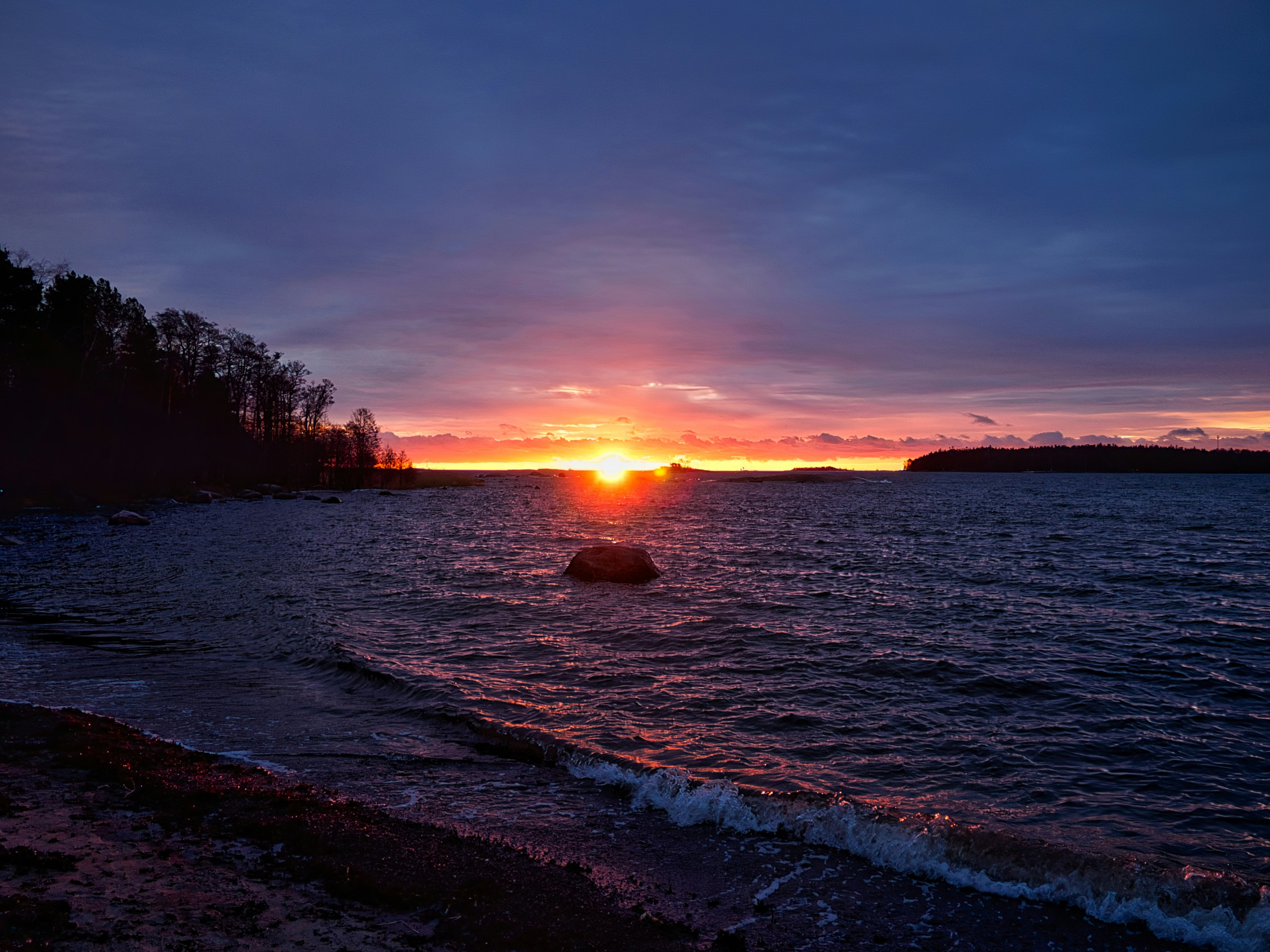 Sunset over a calm ocean with rocky shore.