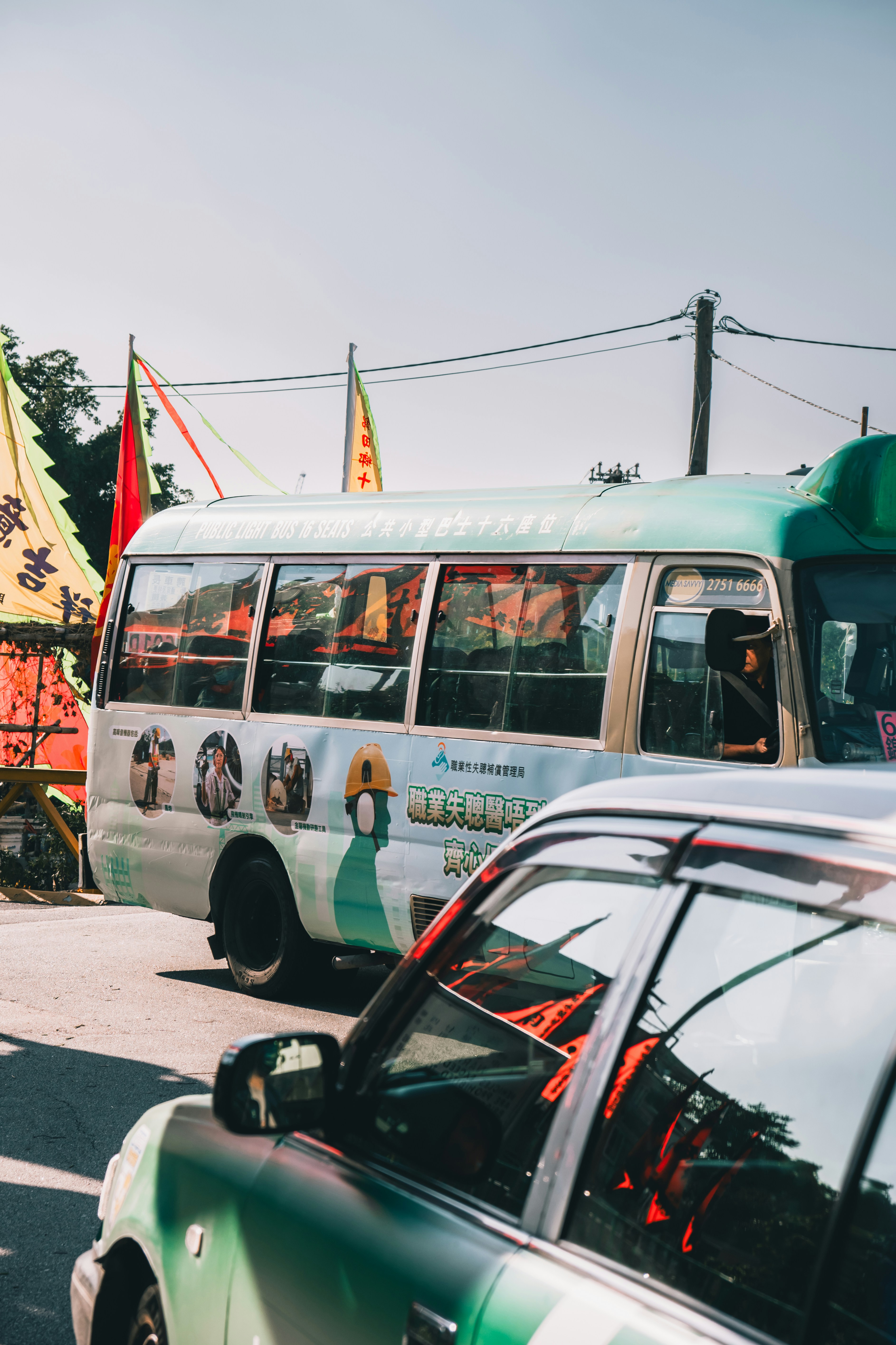 A light blue minibus and a car on a street.