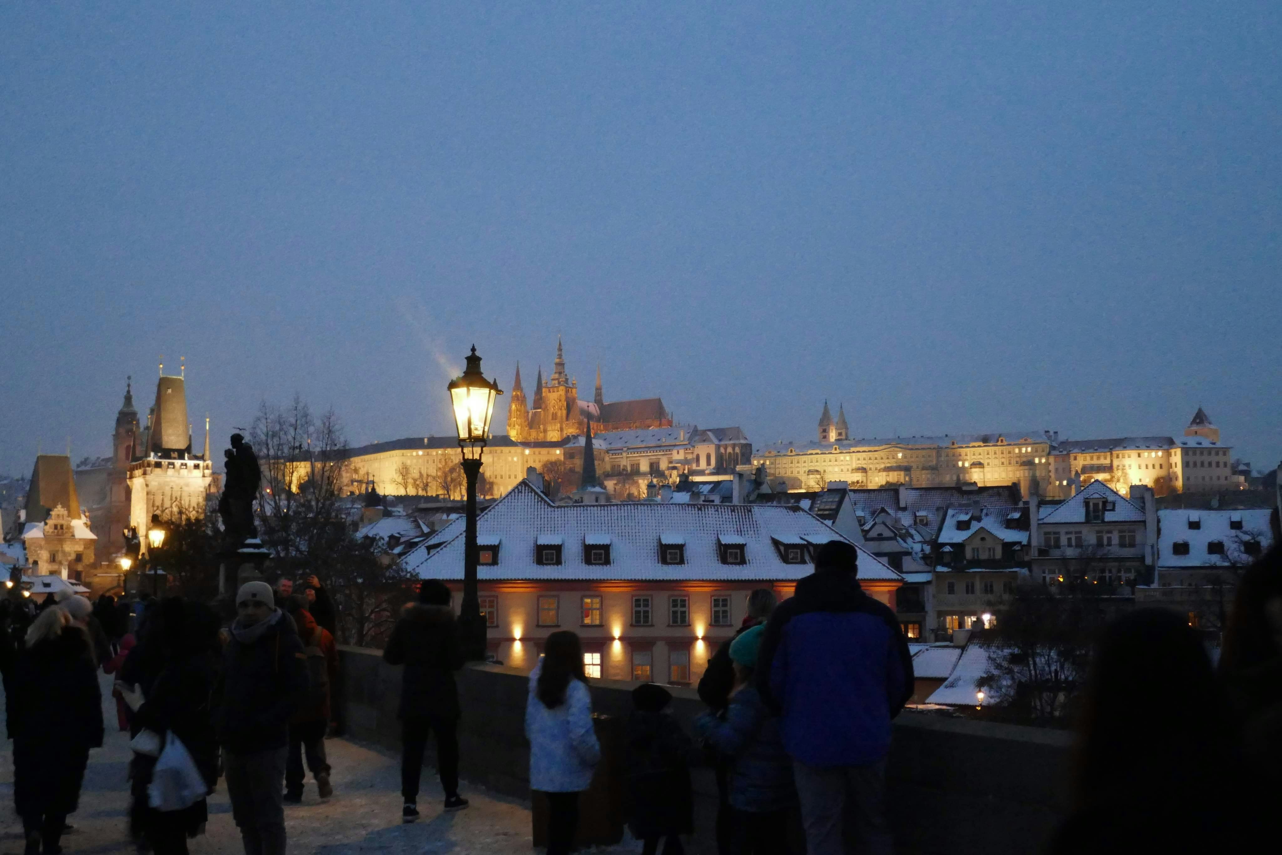 Des gens marchant sur un pont enneigé en direction de bâtiments illuminés.