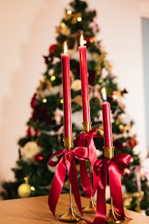 Three red candles with ribbons before christmas tree