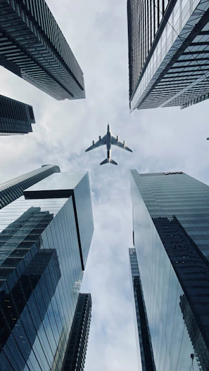 Airplane flying between tall city skyscrapers.