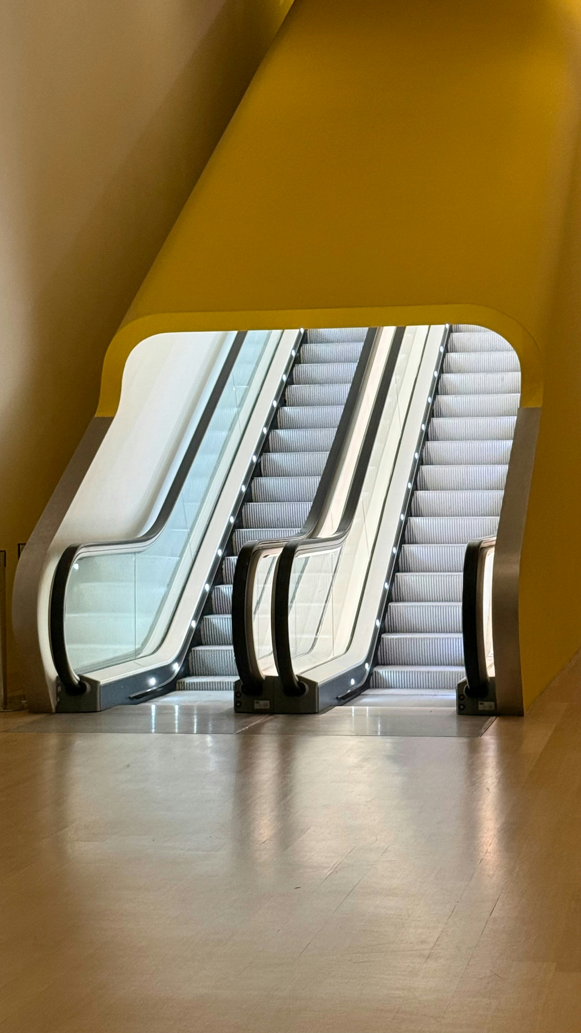 Two escalators ascend within a yellow architectural structure.
