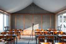 Empty classroom with tables, chairs, and a tripod camera.