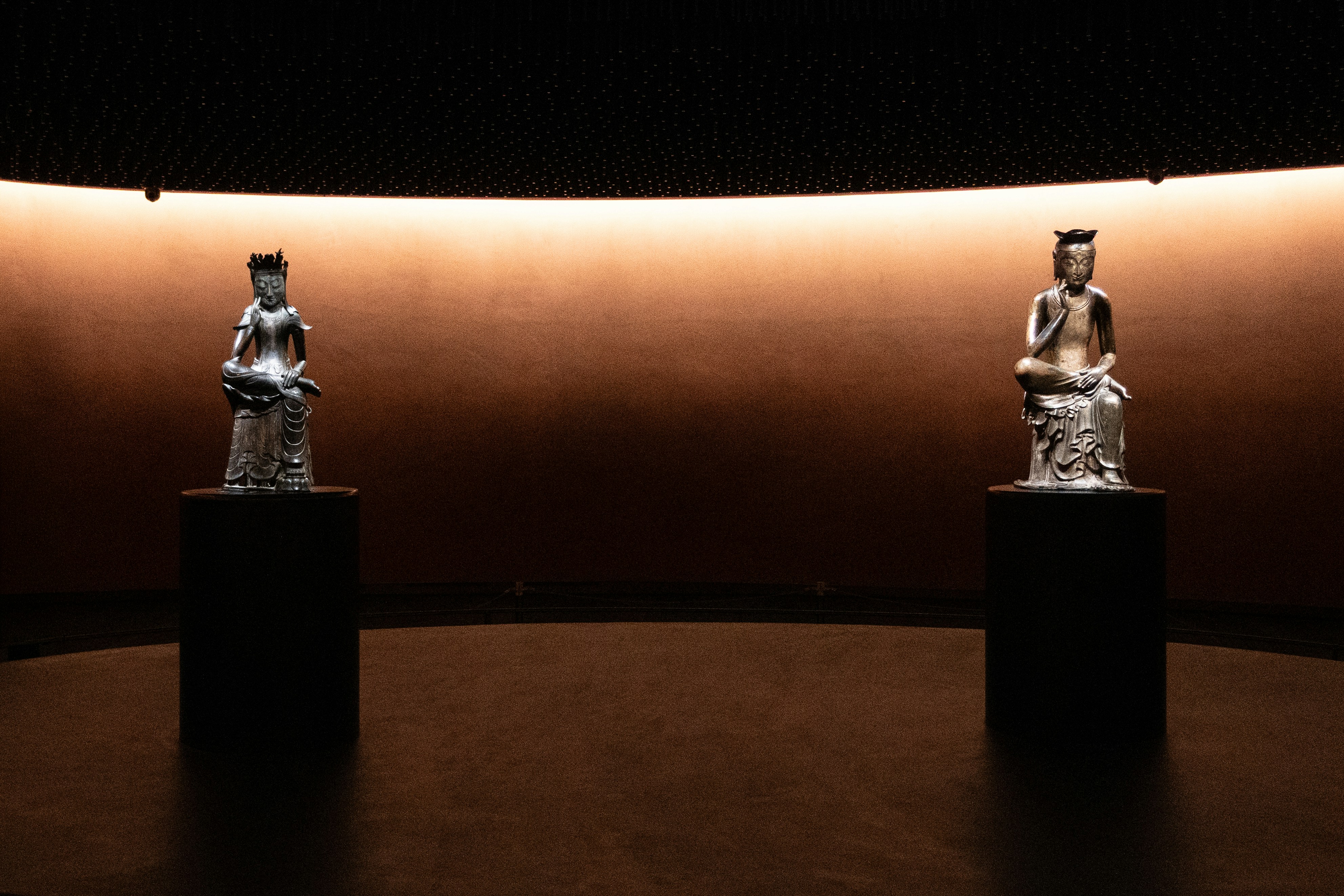 Two statues displayed on pedestals in a dimly lit room.