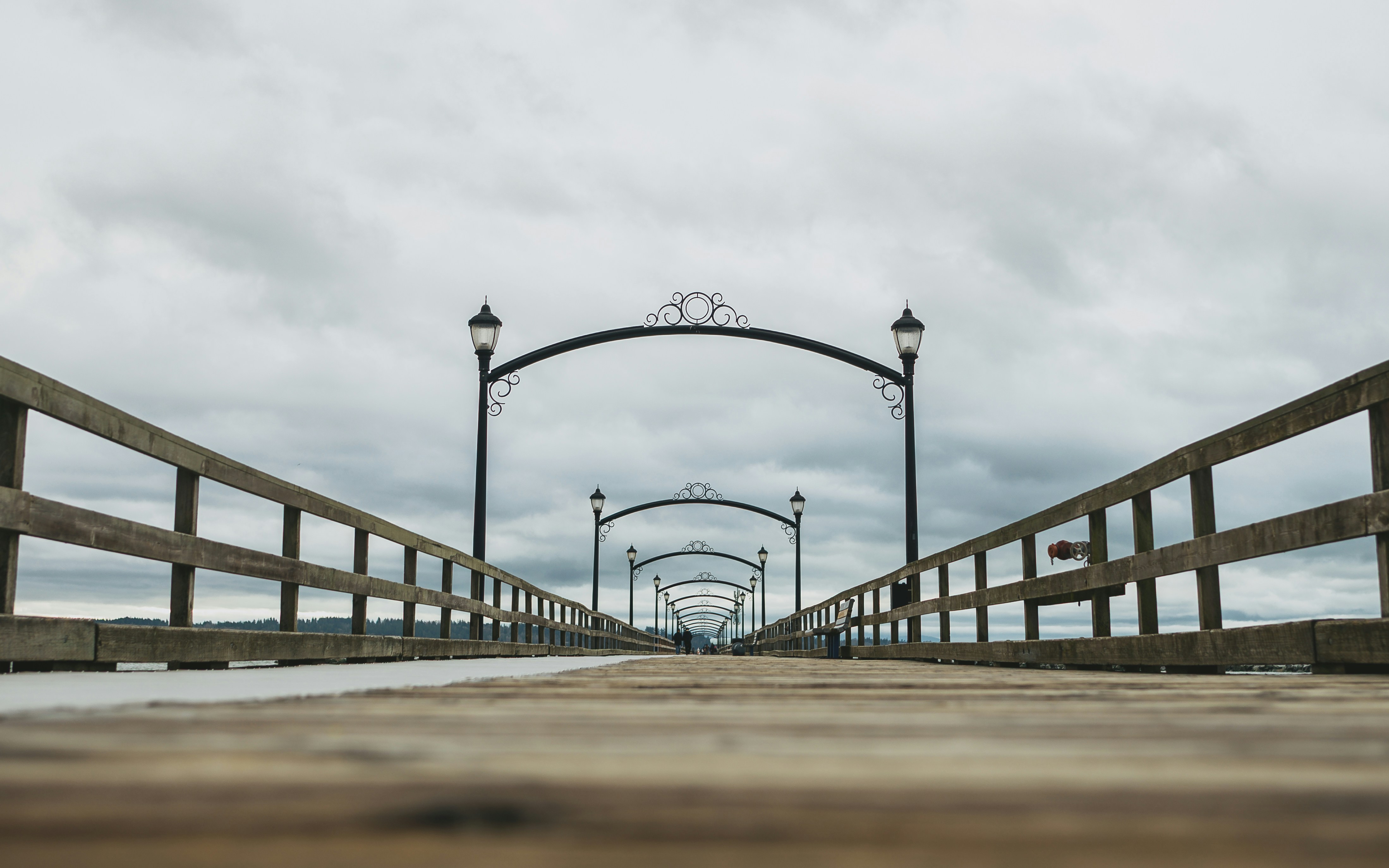 Wooden pier with arched lampposts under cloudy sky