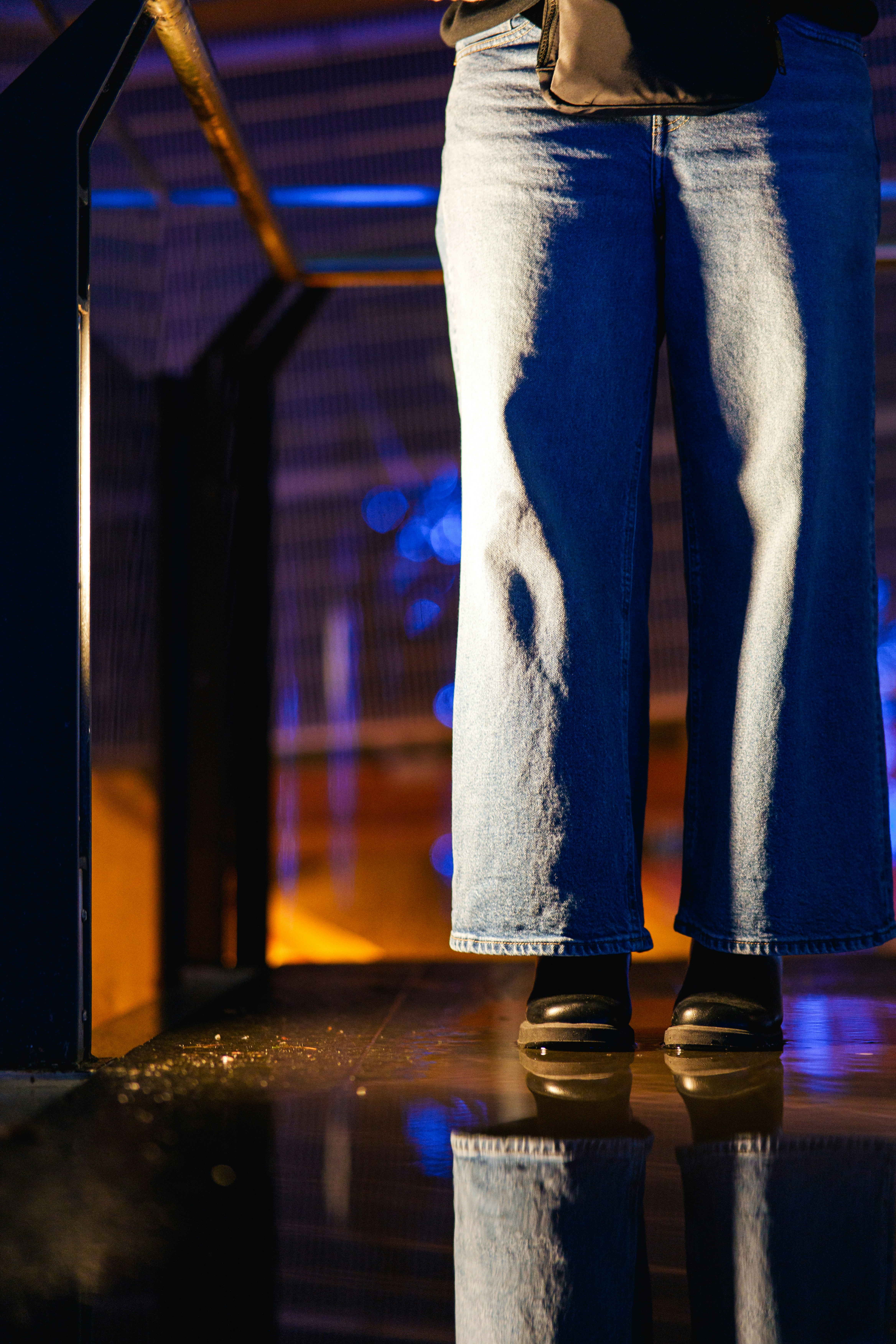 Person standing near a reflective surface with blue lights.