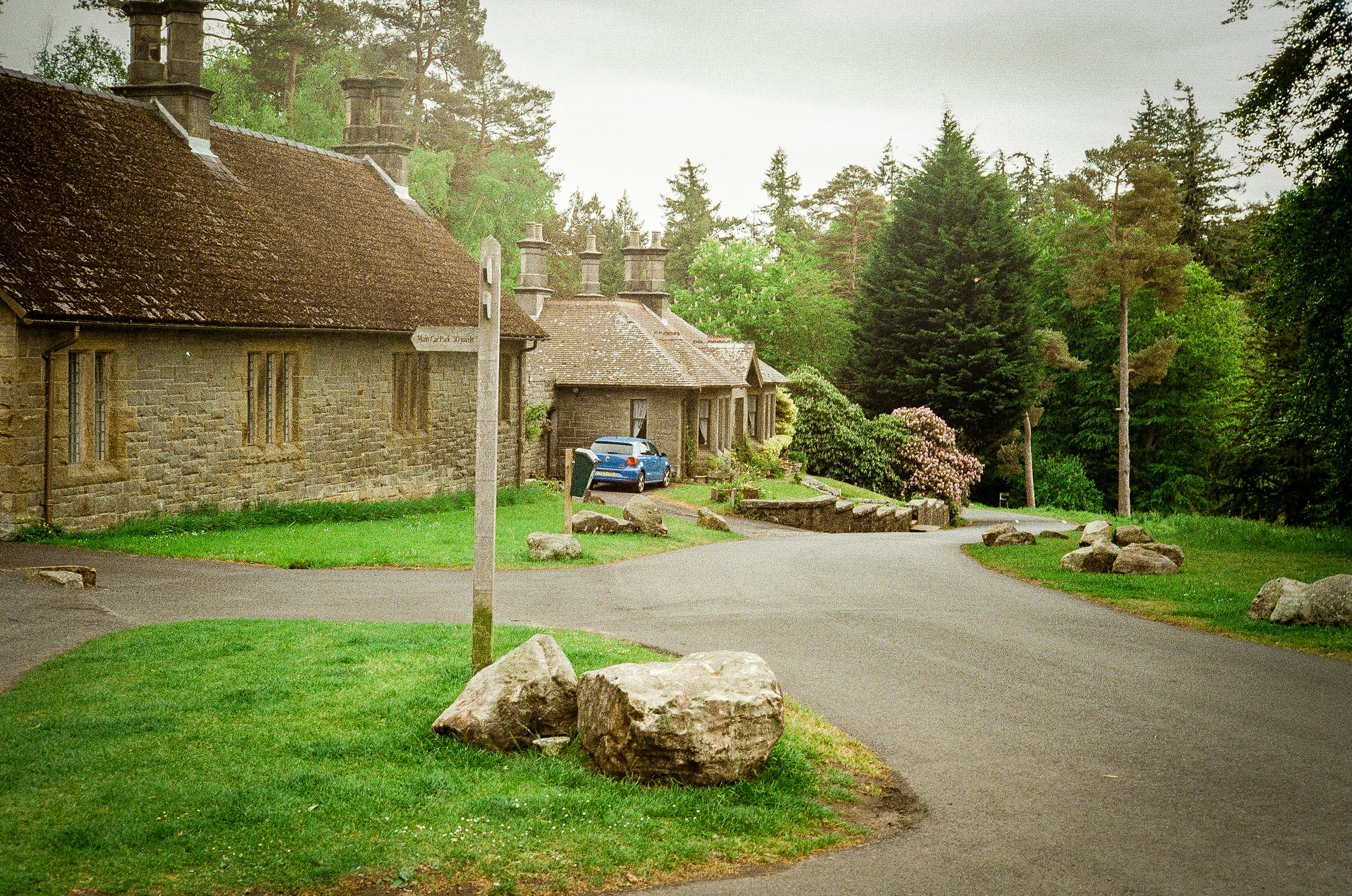 Stone building with blue car in wooded area.