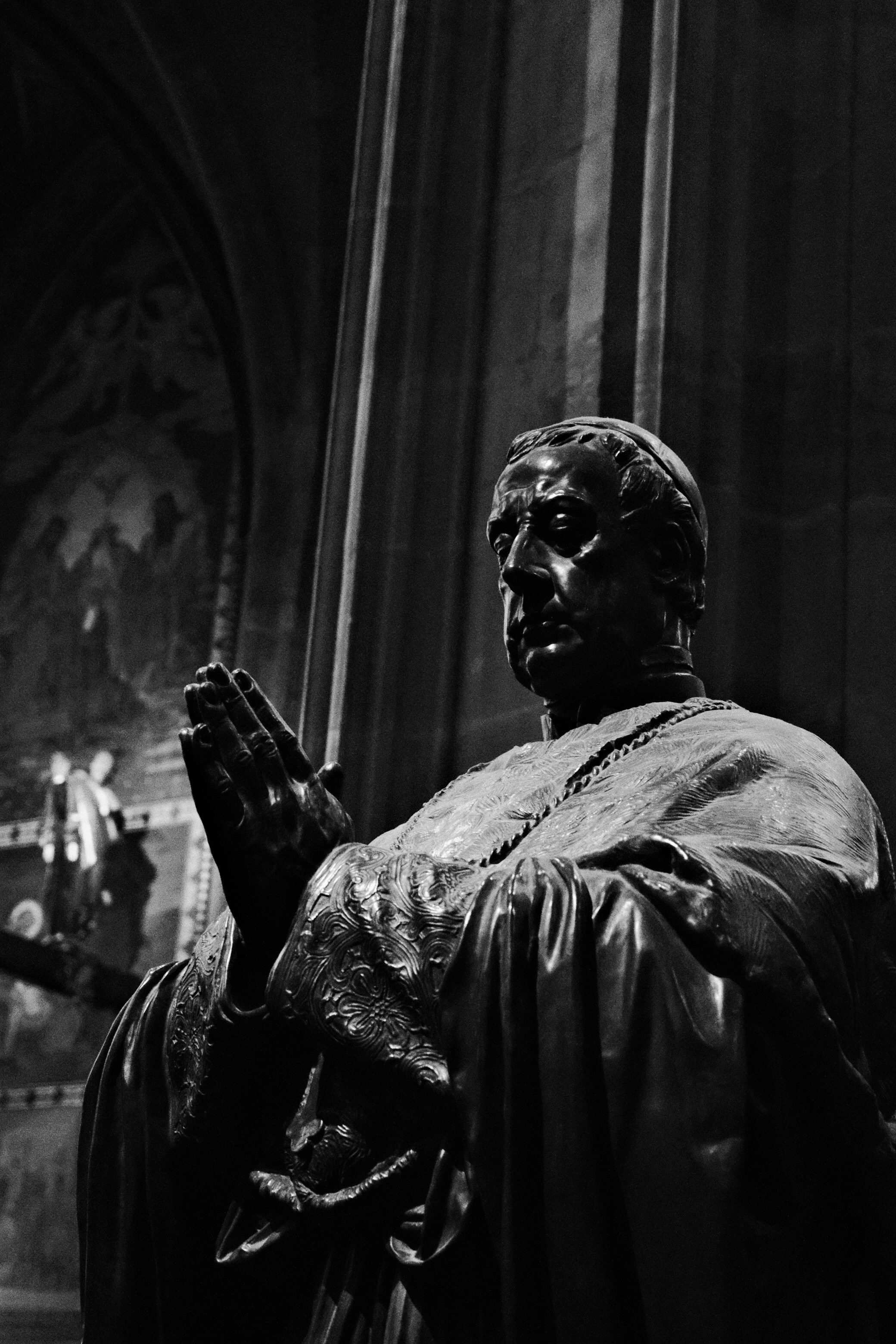 A black and white statue of a man praying.