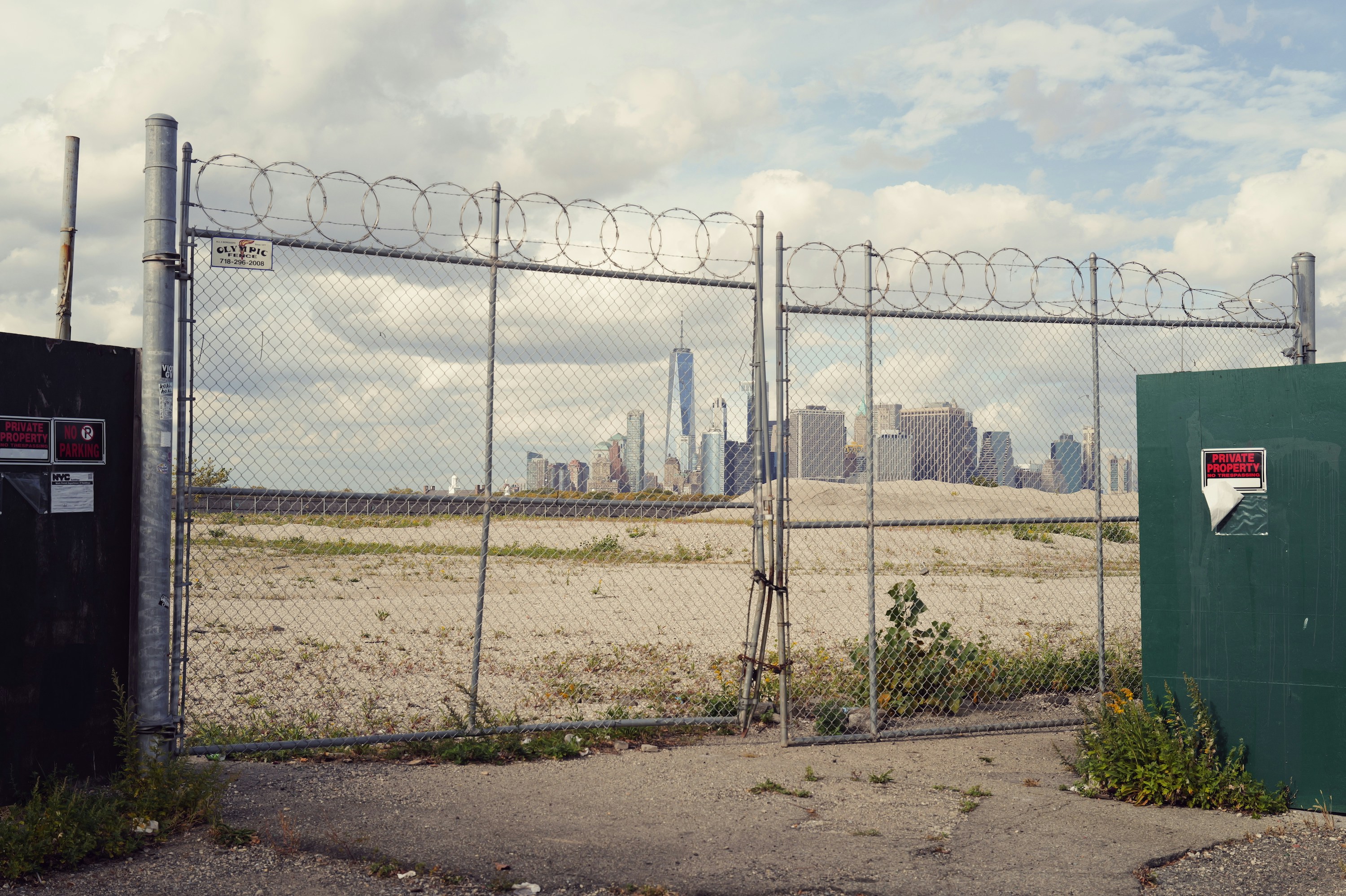 Chain-link fence with barbed wire and cityscape beyond.