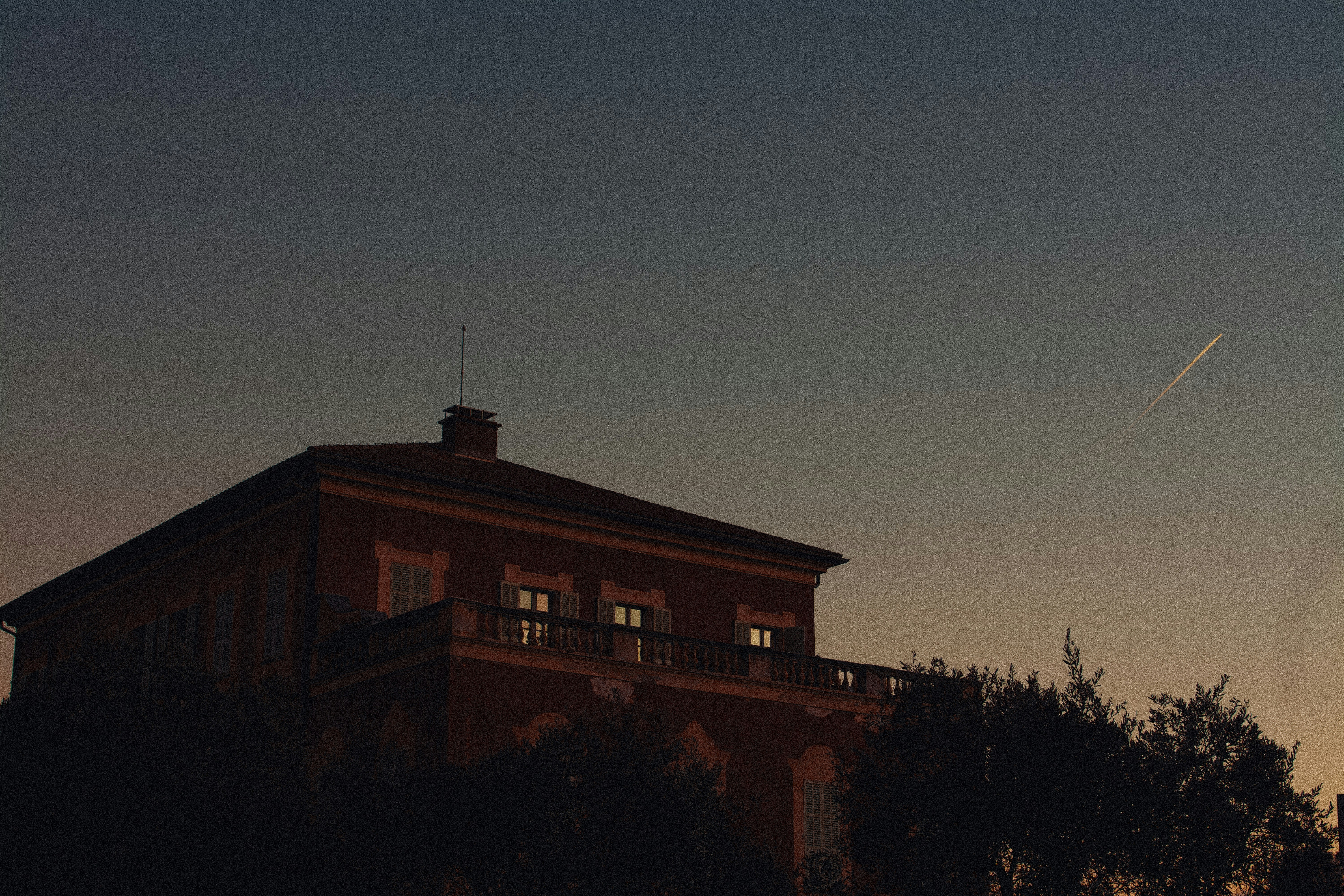 A house silhouetted against a dusky sky with a contrail.