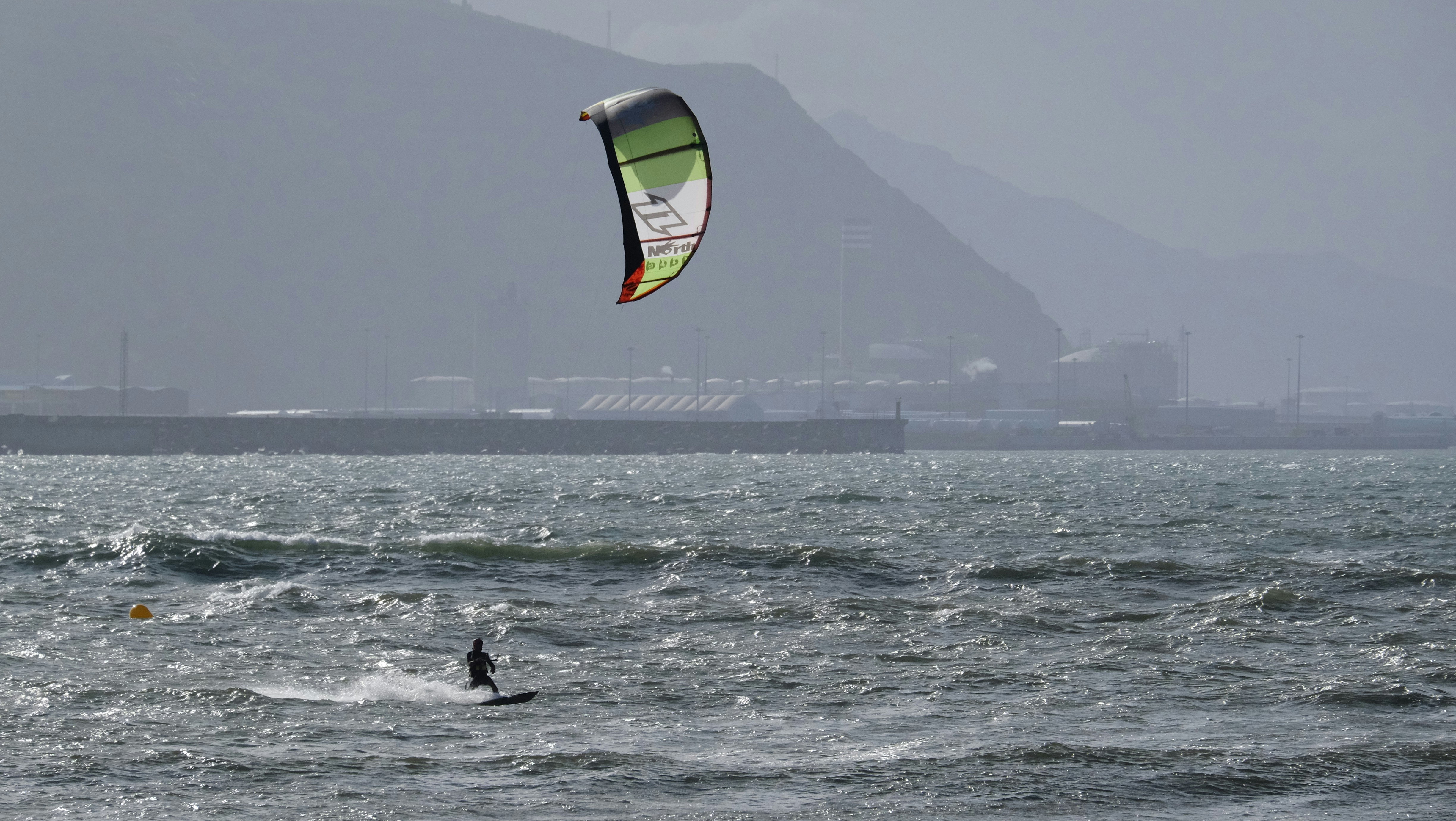 Kitesurfer riding waves with mountains in background