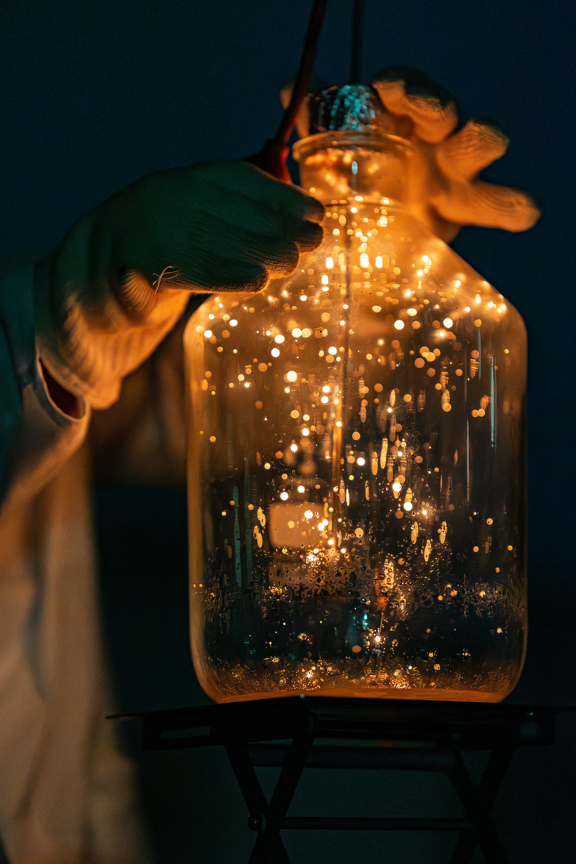 Gloved hands hold a glass jar filled with glowing lights.