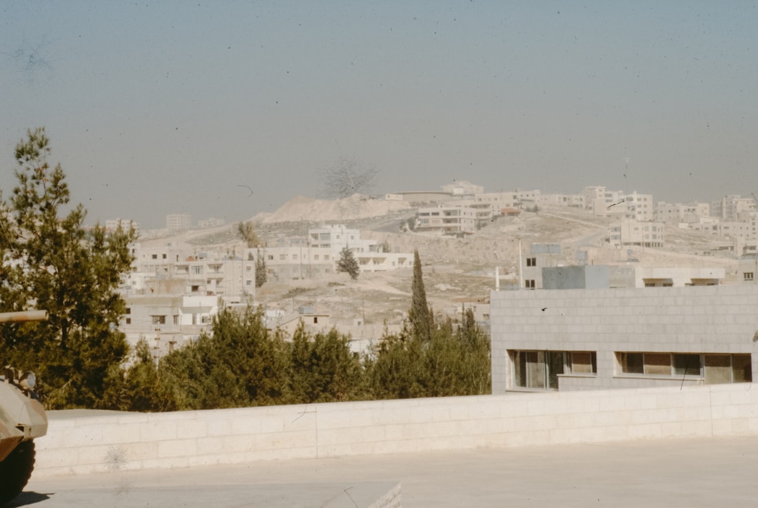 War-damaged buildings on a dusty hillside under a hazy sky — symbolizing the ongoing Middle East conflict between Israel, Iran, and US-backed forces in 2025