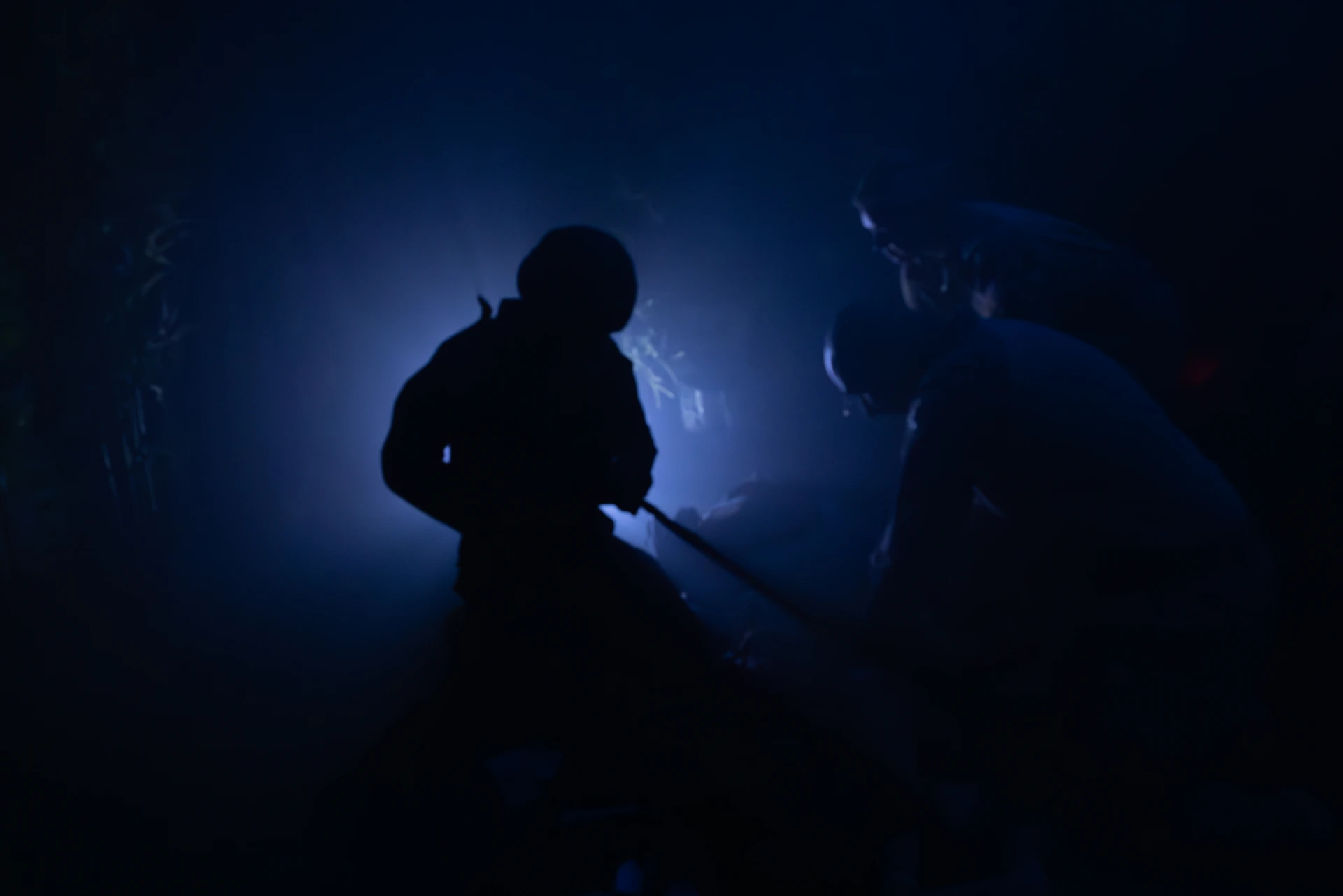 Two silhouetted figures in a dark, foggy environment.