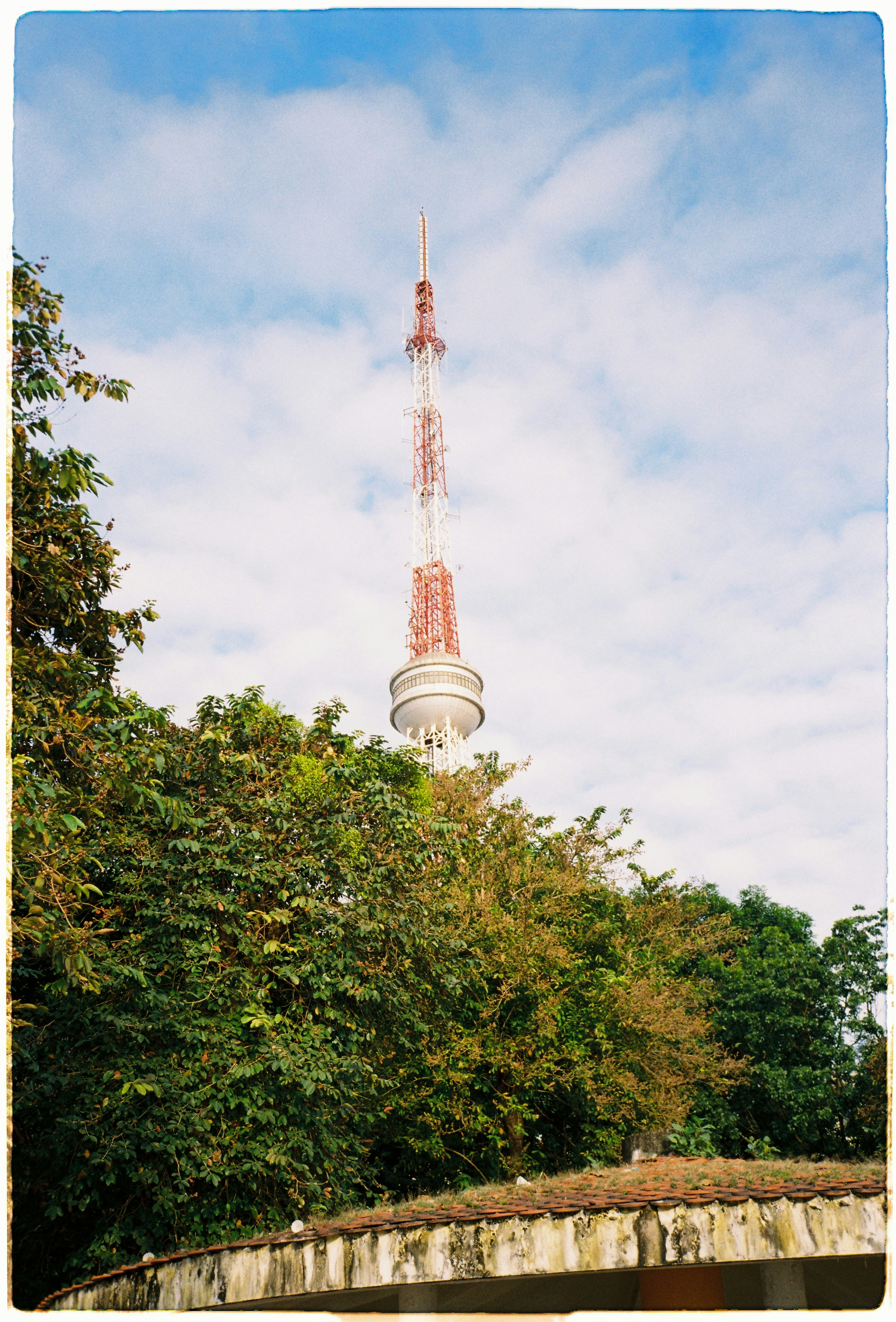 Tall radio tower behind green trees and blue sky