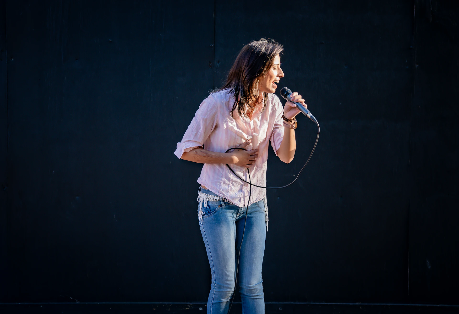 Woman singing into a microphone against a dark background