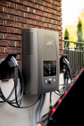 Electric car charger mounted on brick wall outdoors.