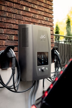Electric car charger mounted on brick wall outdoors.
