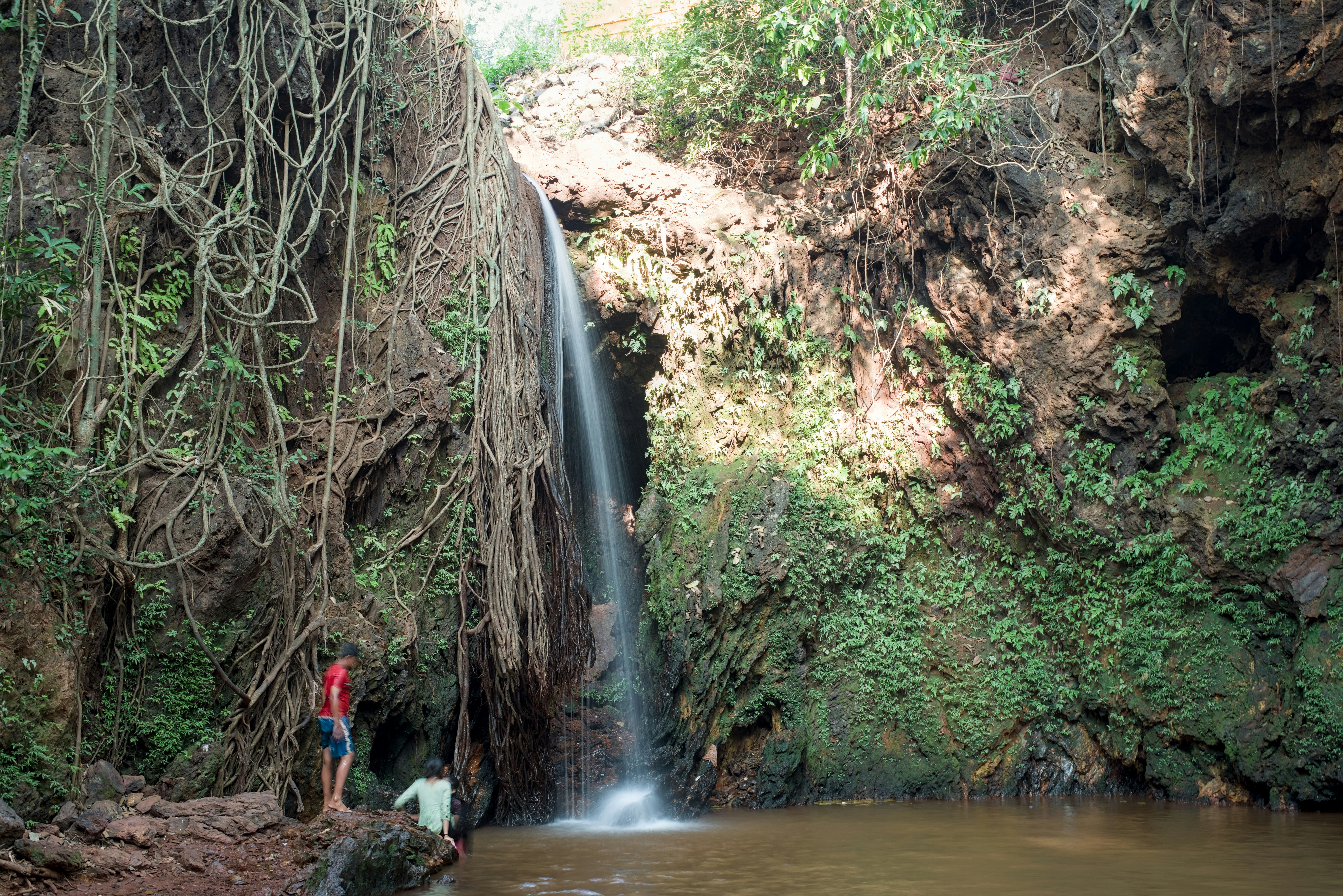 A waterfall cascades into a pool with people nearby.